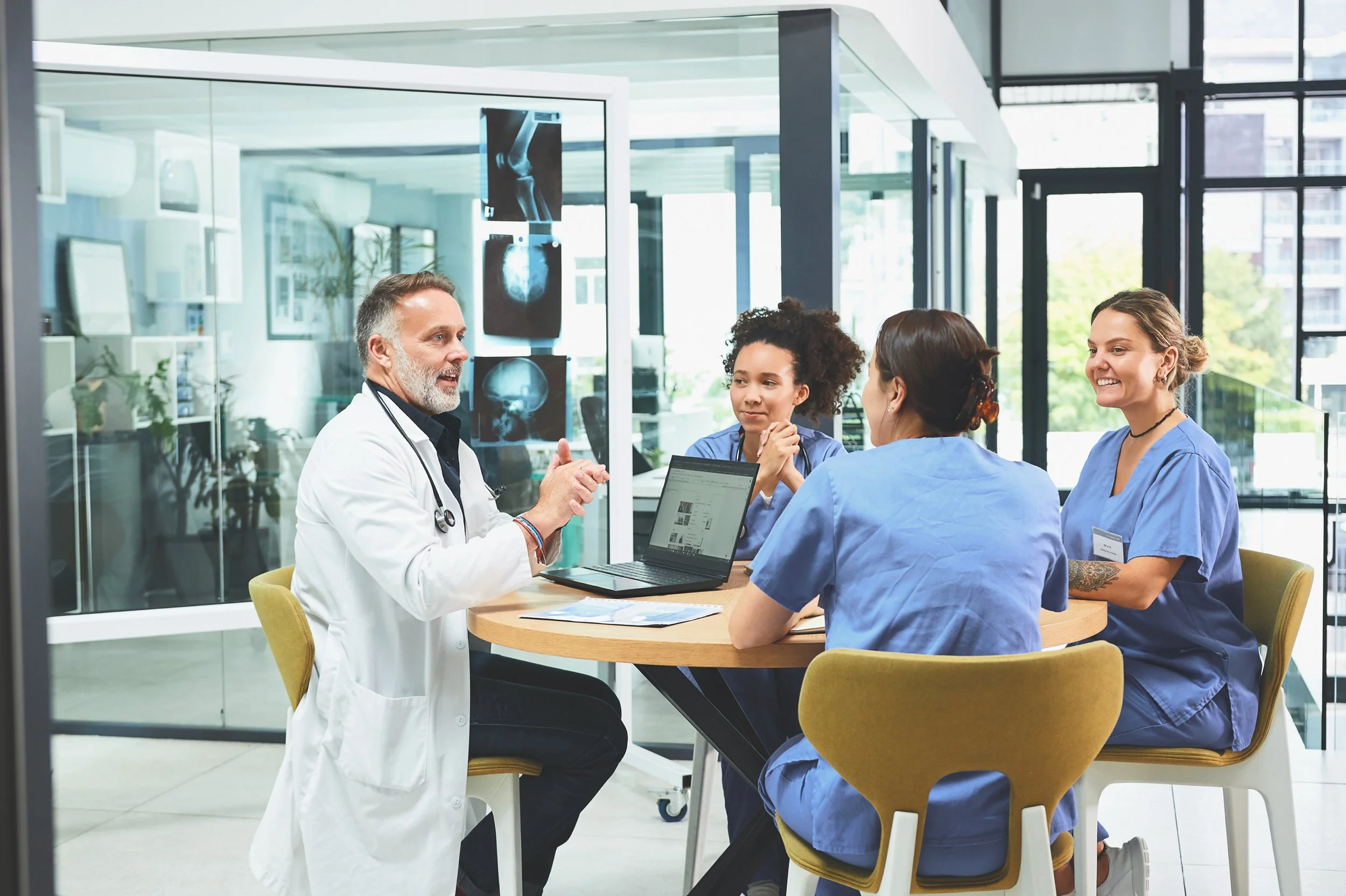 Medical team having a discussion in a modern hospital conference room with X-ray and MRI images on the wall.