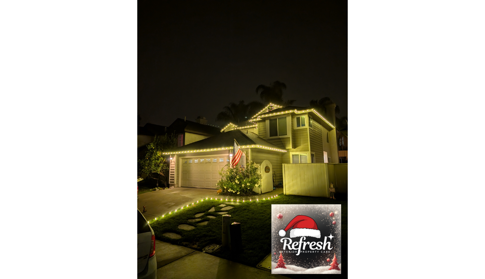 A house decorated with Christmas lights at night, featuring a garage door, an American flag, a bush with flowers, and a small white planter. There is a driveway with stepping stones and a lawn, with a logo of a Santa hat and Christmas trees in the bottom right corner.