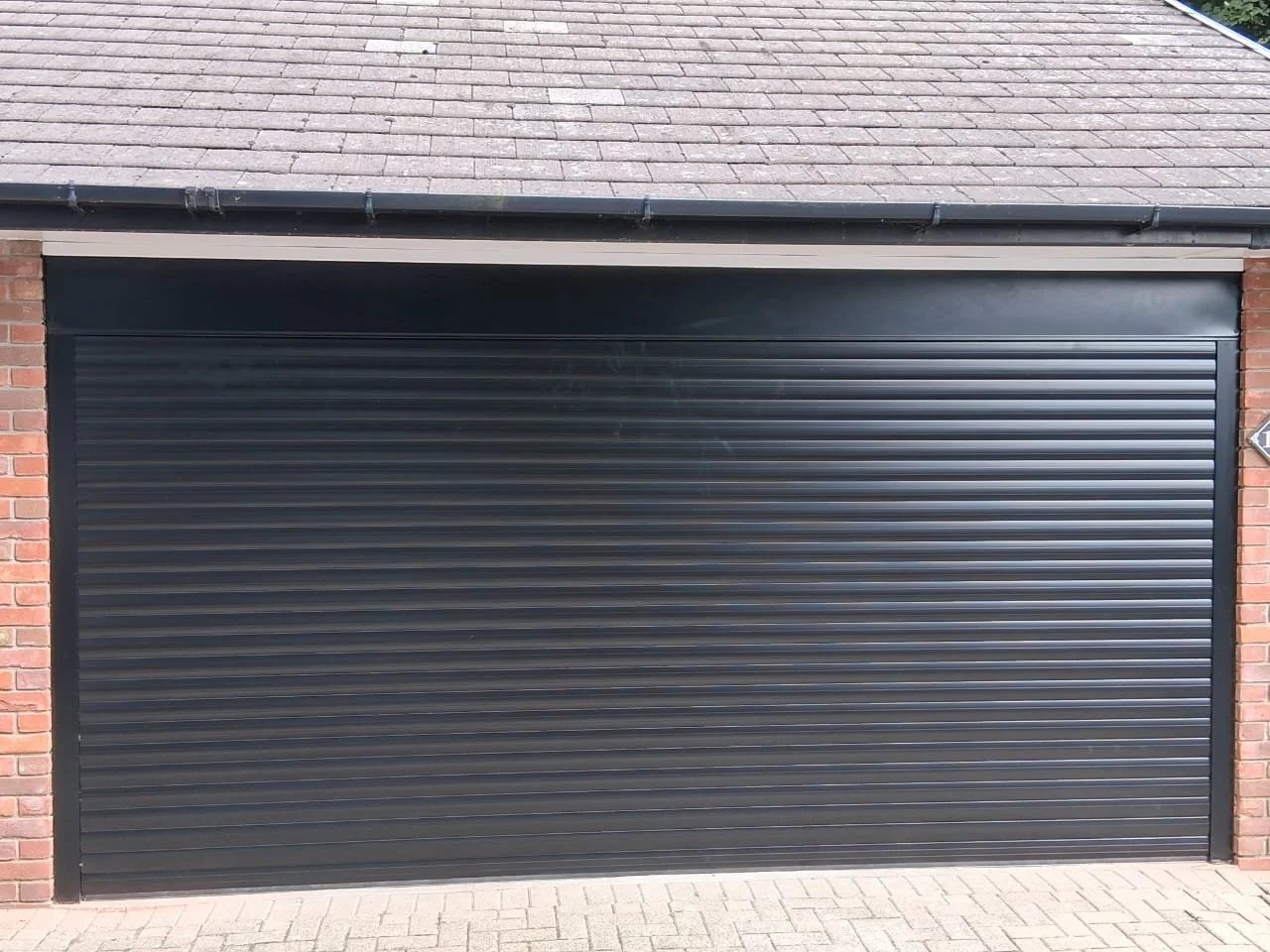 Black roll-up garage door on a brick house with a shingled roof.