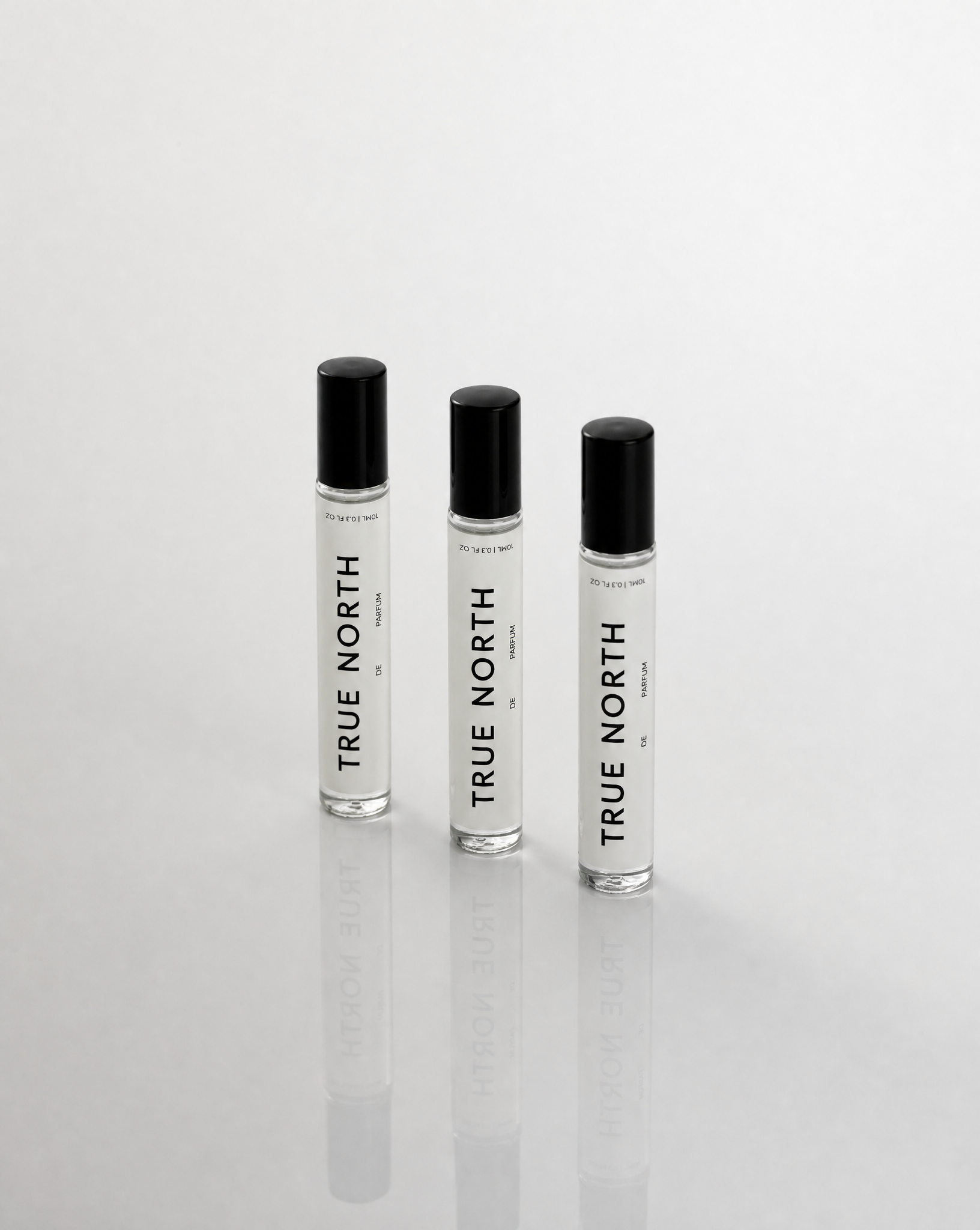Three perfume bottles with white labels and black caps, arranged in a row against a white background.