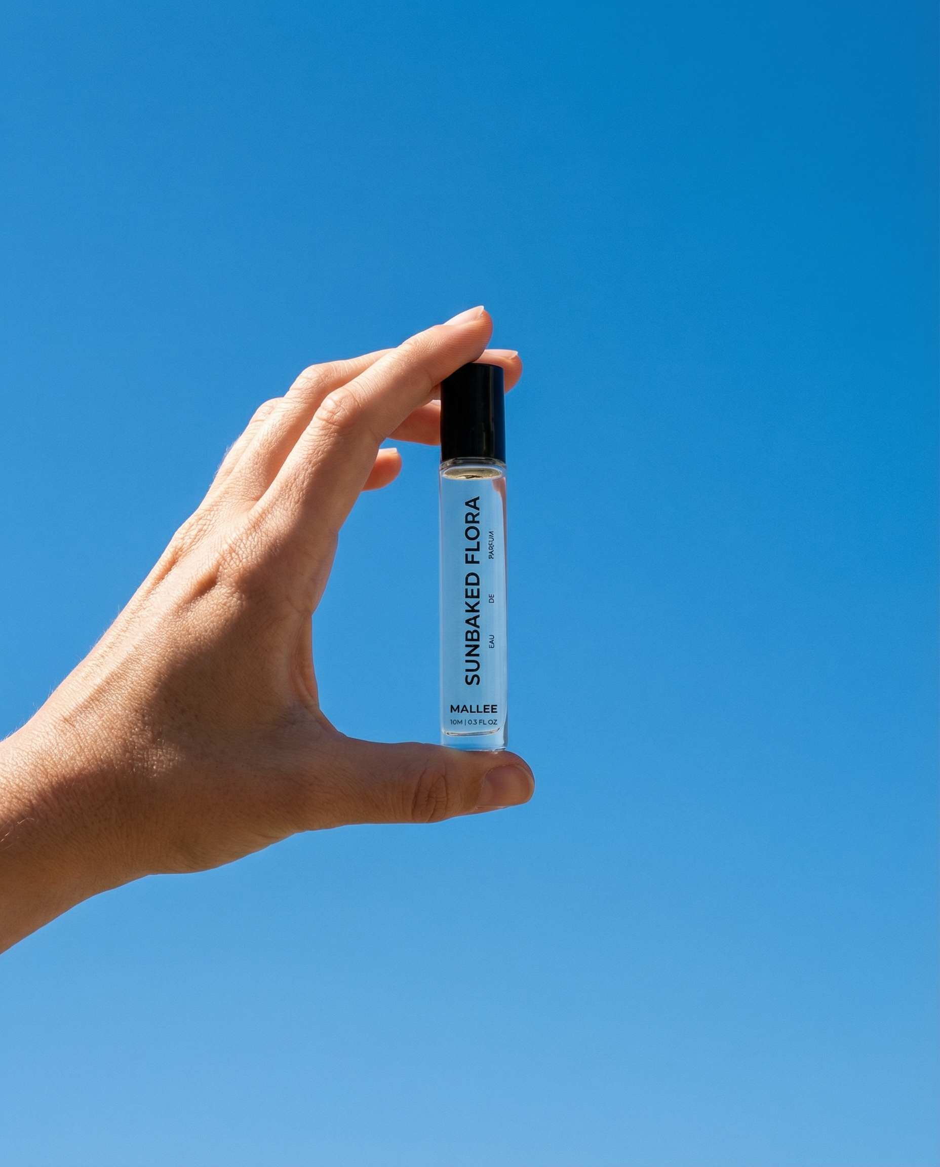A hand holding a small vial or test tube against a clear blue sky.