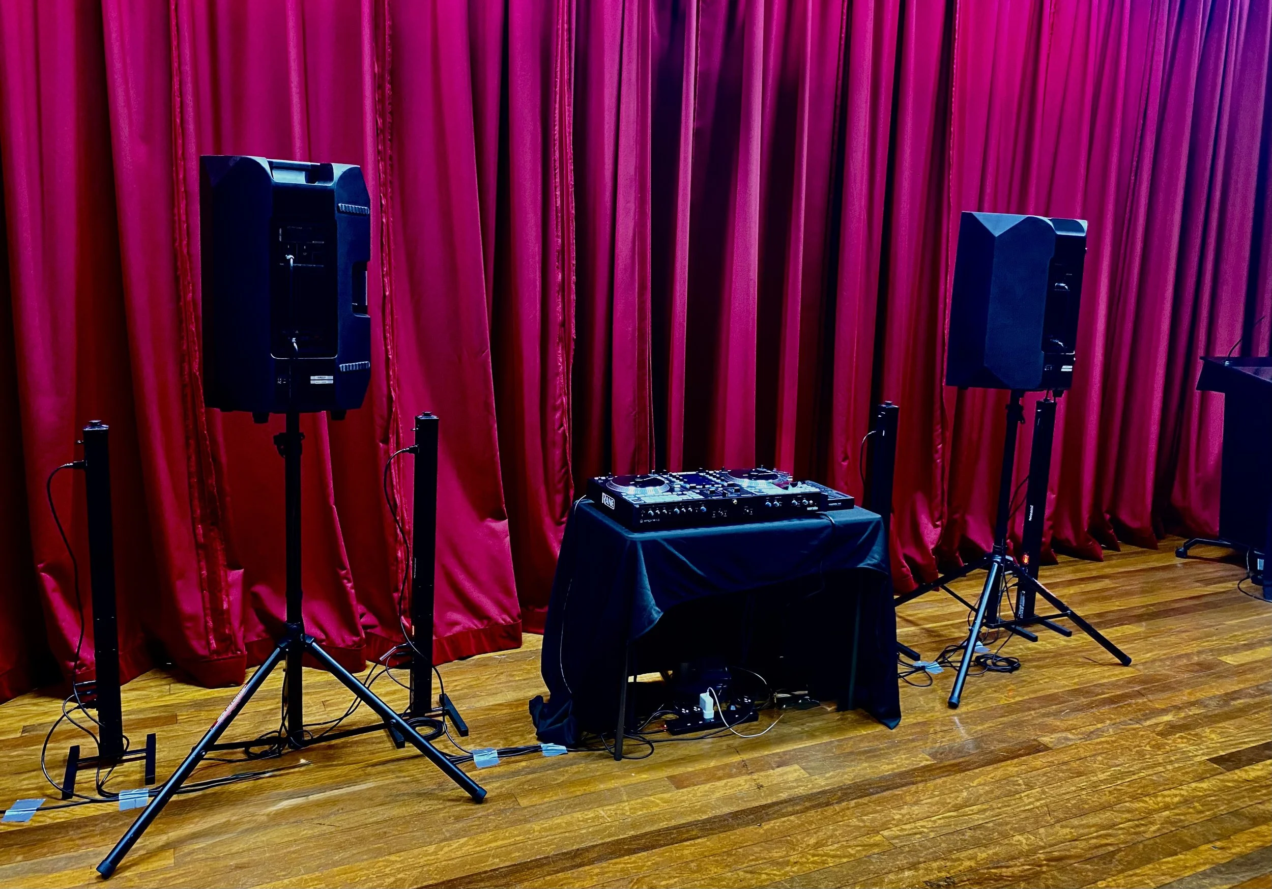 DJ equipment and speakers set up in front of red stage curtains.