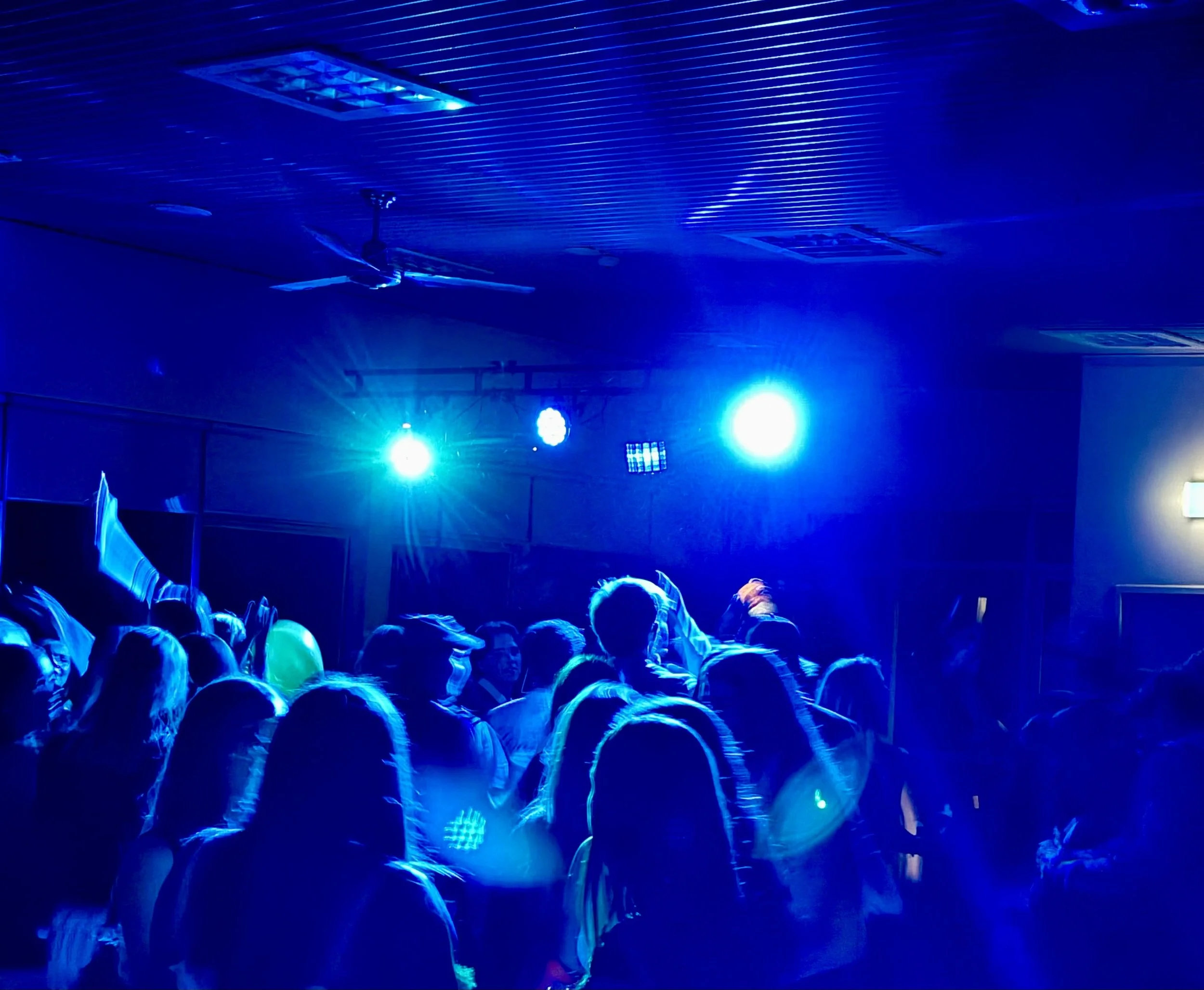 A crowd of people with blue lighting overhead, possibly in a nightclub or concert setting.