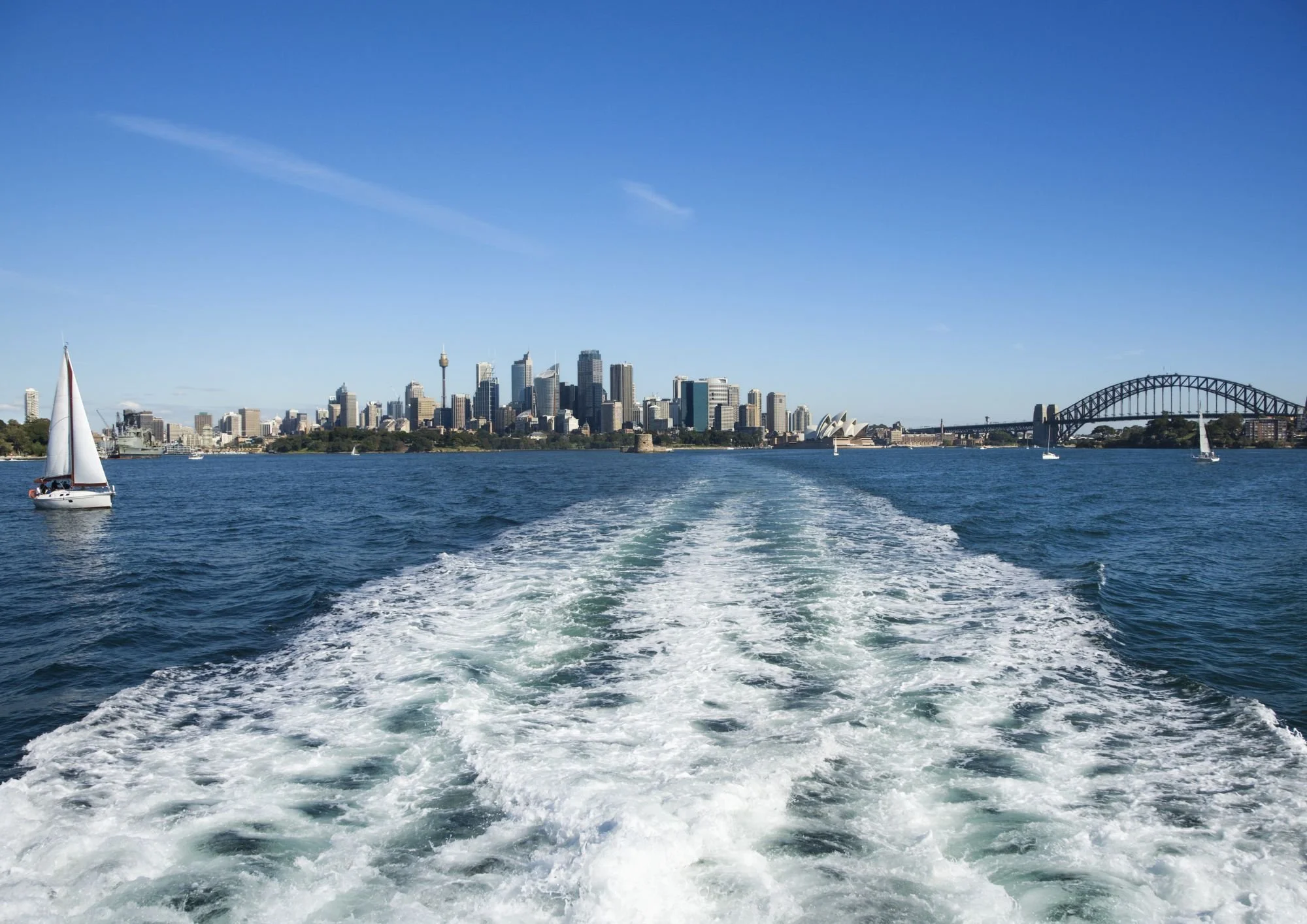 View of Sydney skyline from a boat, with sailboats and the Sydney Harbour Bridge in the background.