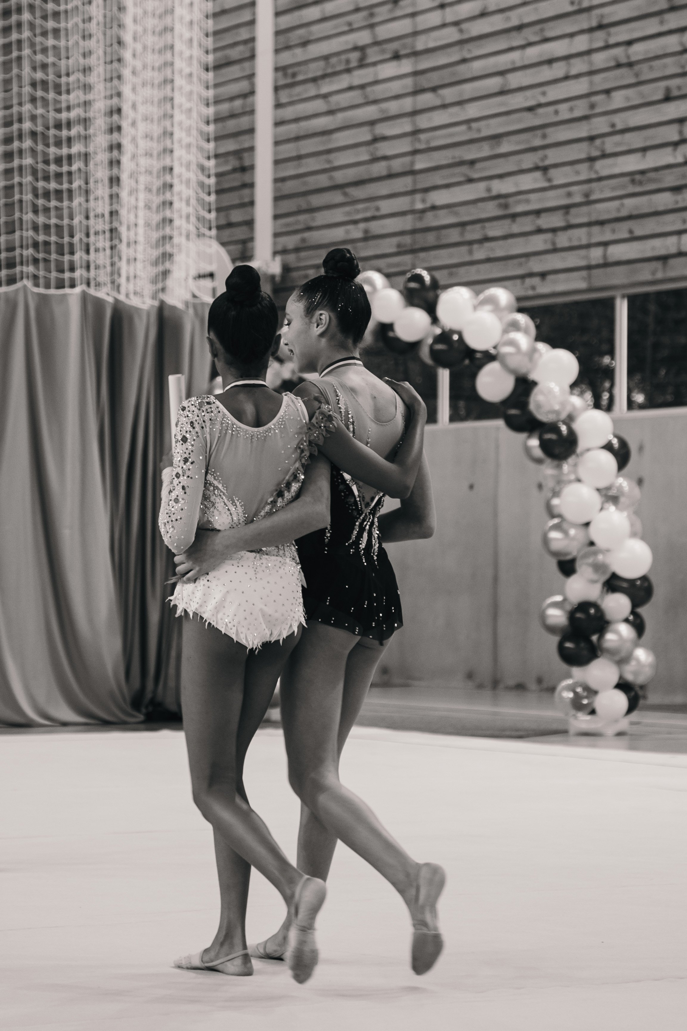 Deux jeunes gymnastes en compétition lors d'un événement sportif, habillées en costumes de gymnastique, en train de partager un moment de camaraderie après leur performance.