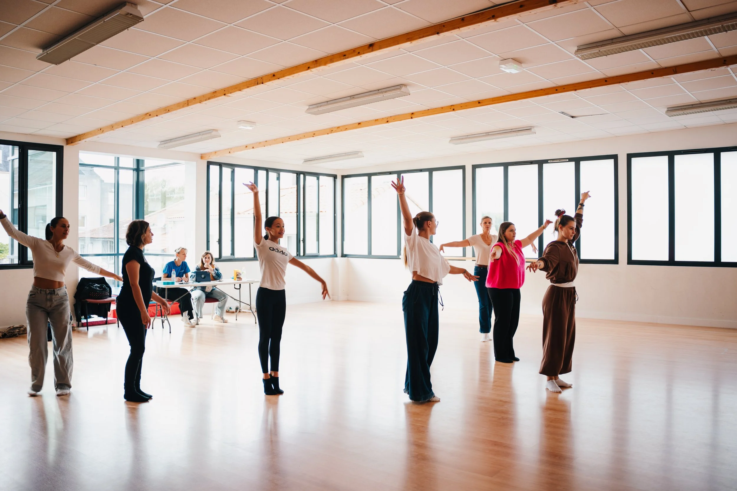Groupe de femmes en train de pratiquer la danse ou la chorégraphie dans une salle de danse lumineuse avec de grandes fenêtres.