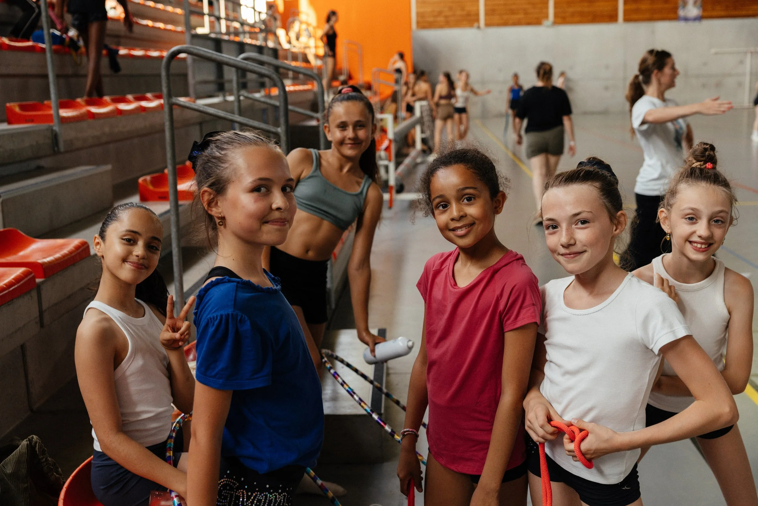 Groupe de jeunes filles dans une salle d'entraînement ou de compétition, certaines avec des cordes à sauter.