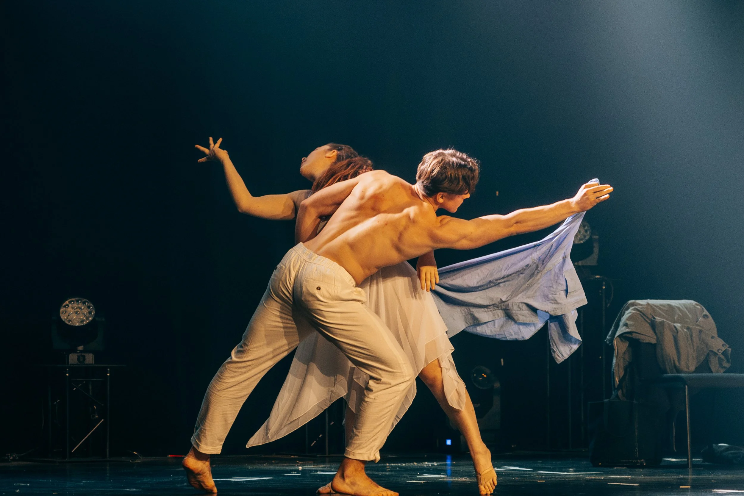Trois danseurs nus et vêtus de vêtements légers en mouvement sur scène, dans une scène d'une performance artistique.