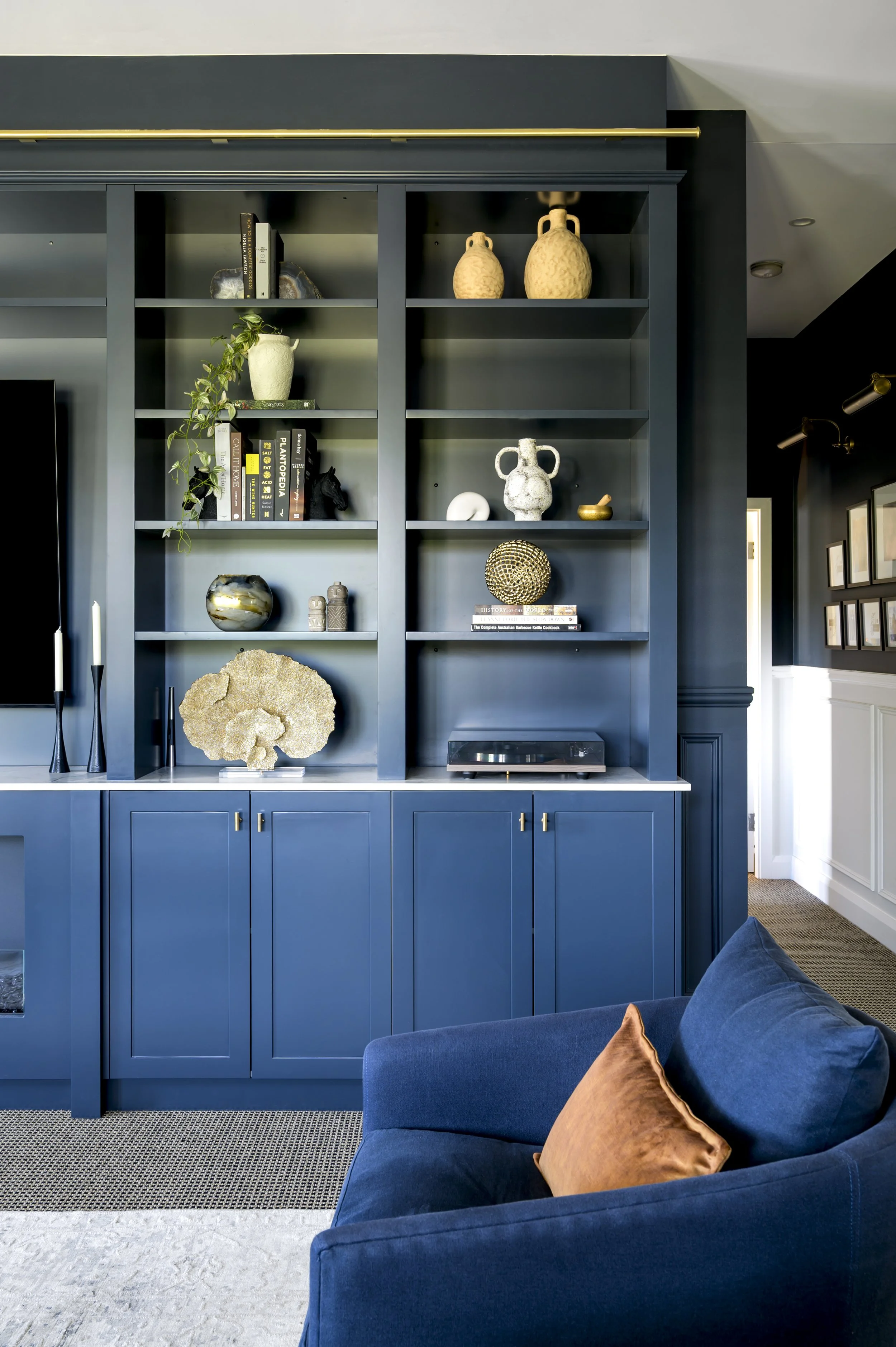A built-in dark blue bookshelf with various decorative items, books, and a turntable, in a modern living room with a blue sofa and a brown cushion.