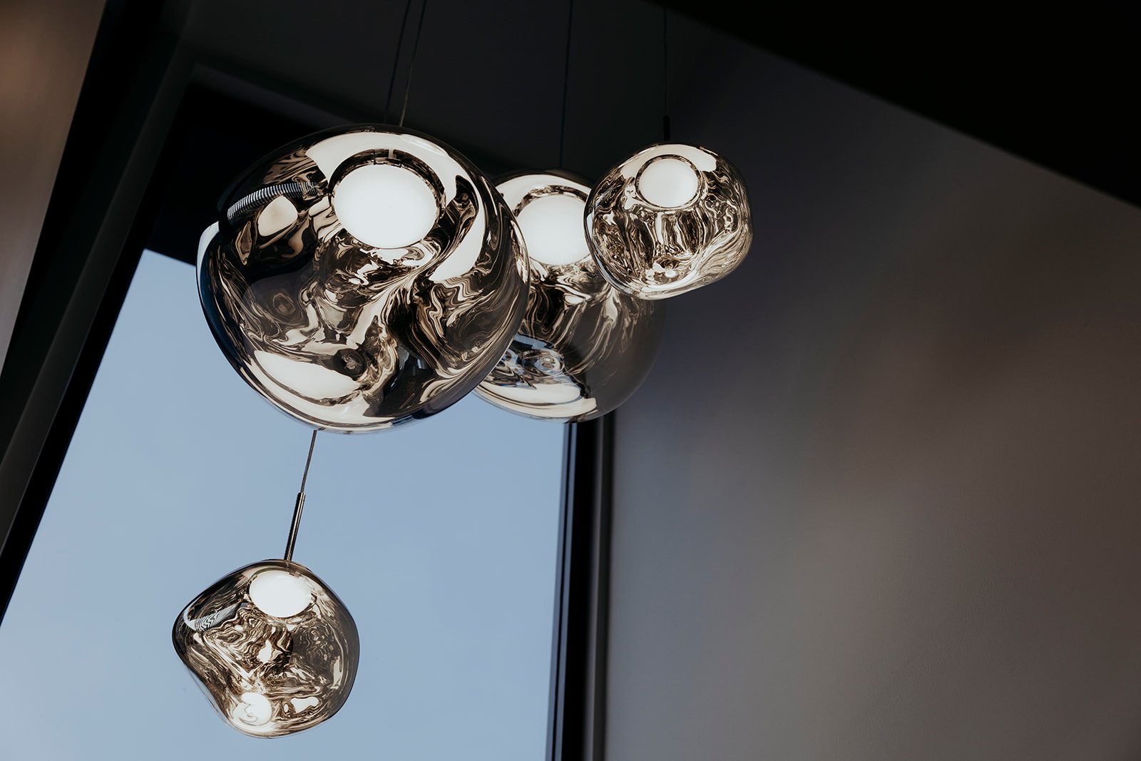 Modern hanging light fixtures with reflective, abstract glass or metal designs attached to a ceiling near a window.