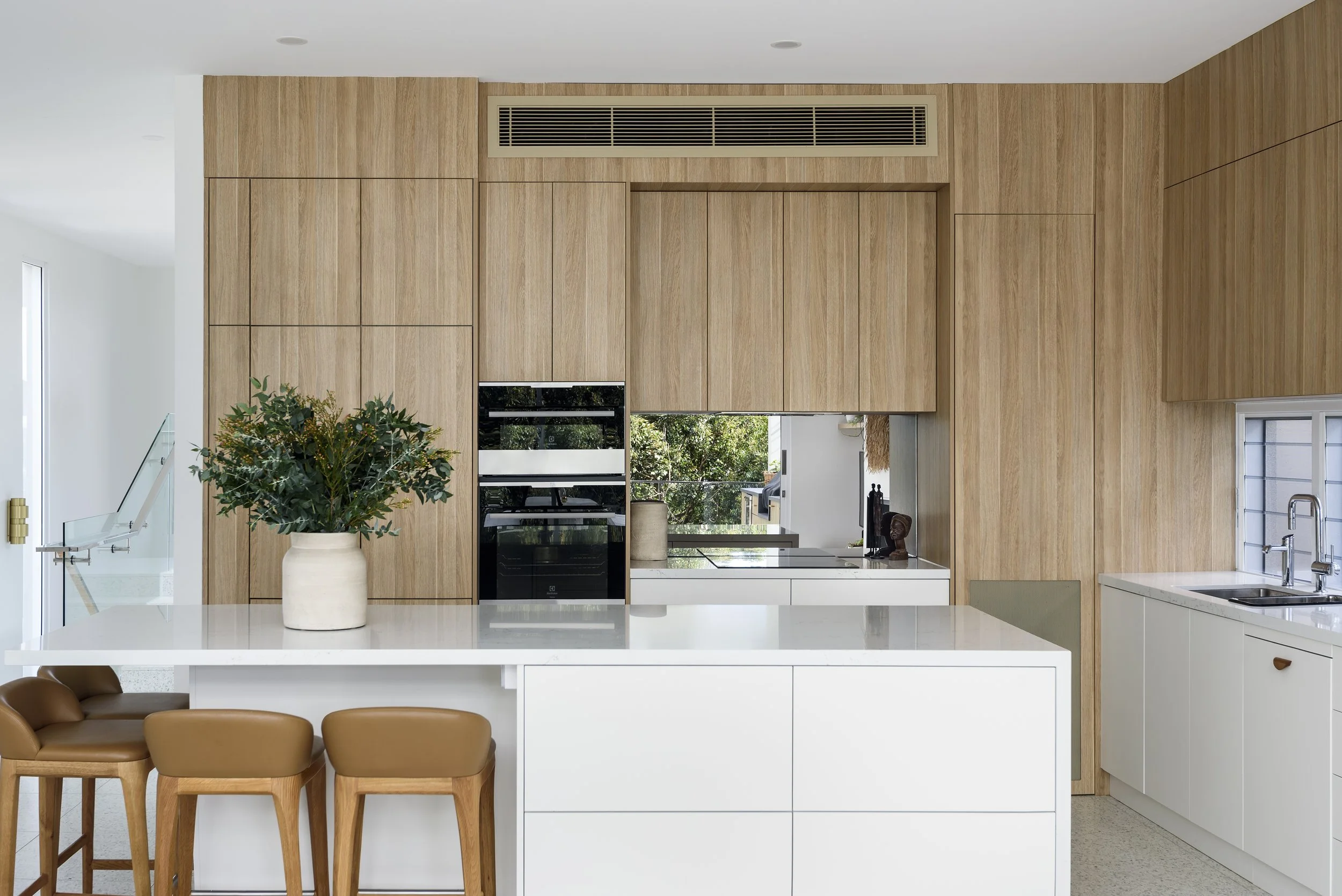 Modern kitchen with white island, wooden cabinets, and black appliances, decorated with potted plant and small sculptures.