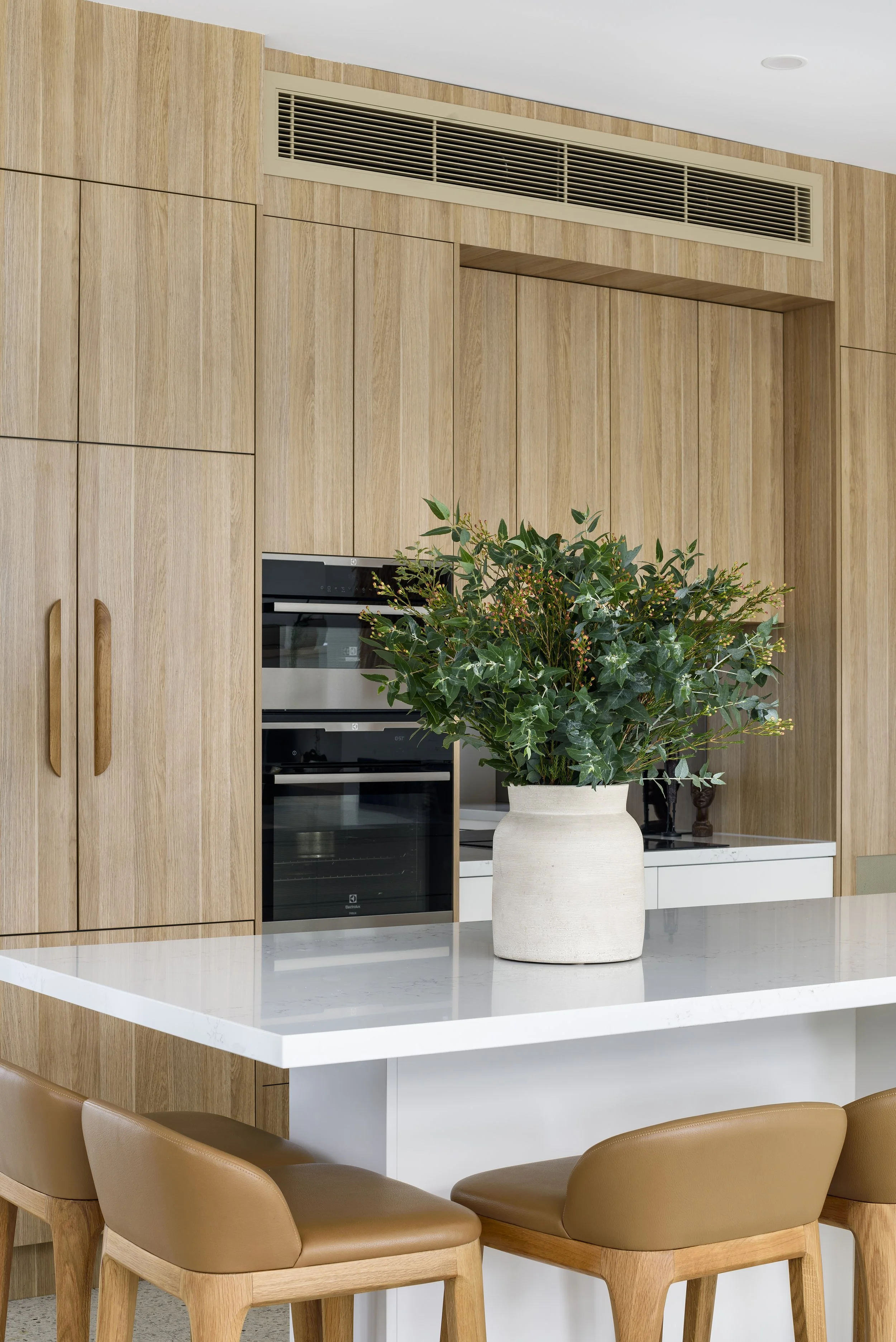 A modern kitchen with a white countertop, a potted green plant on the counter, wood cabinets, and a built-in oven.