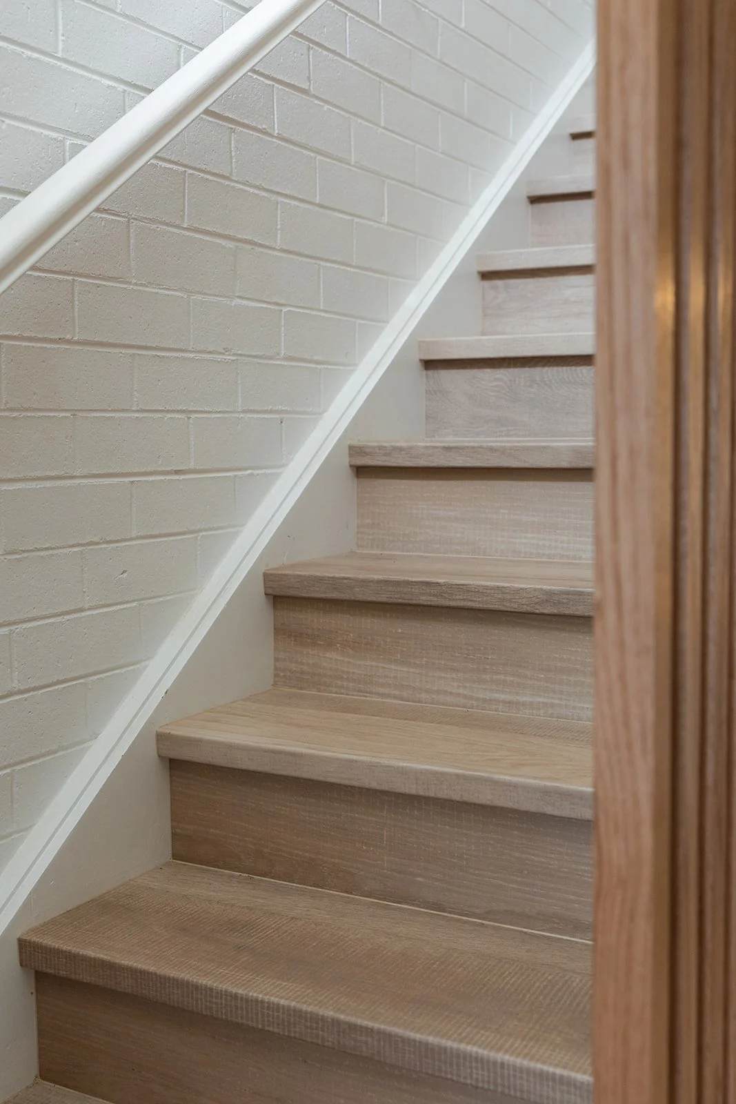 Wooden staircase with a white brick wall on the left and a wooden wall on the right.
