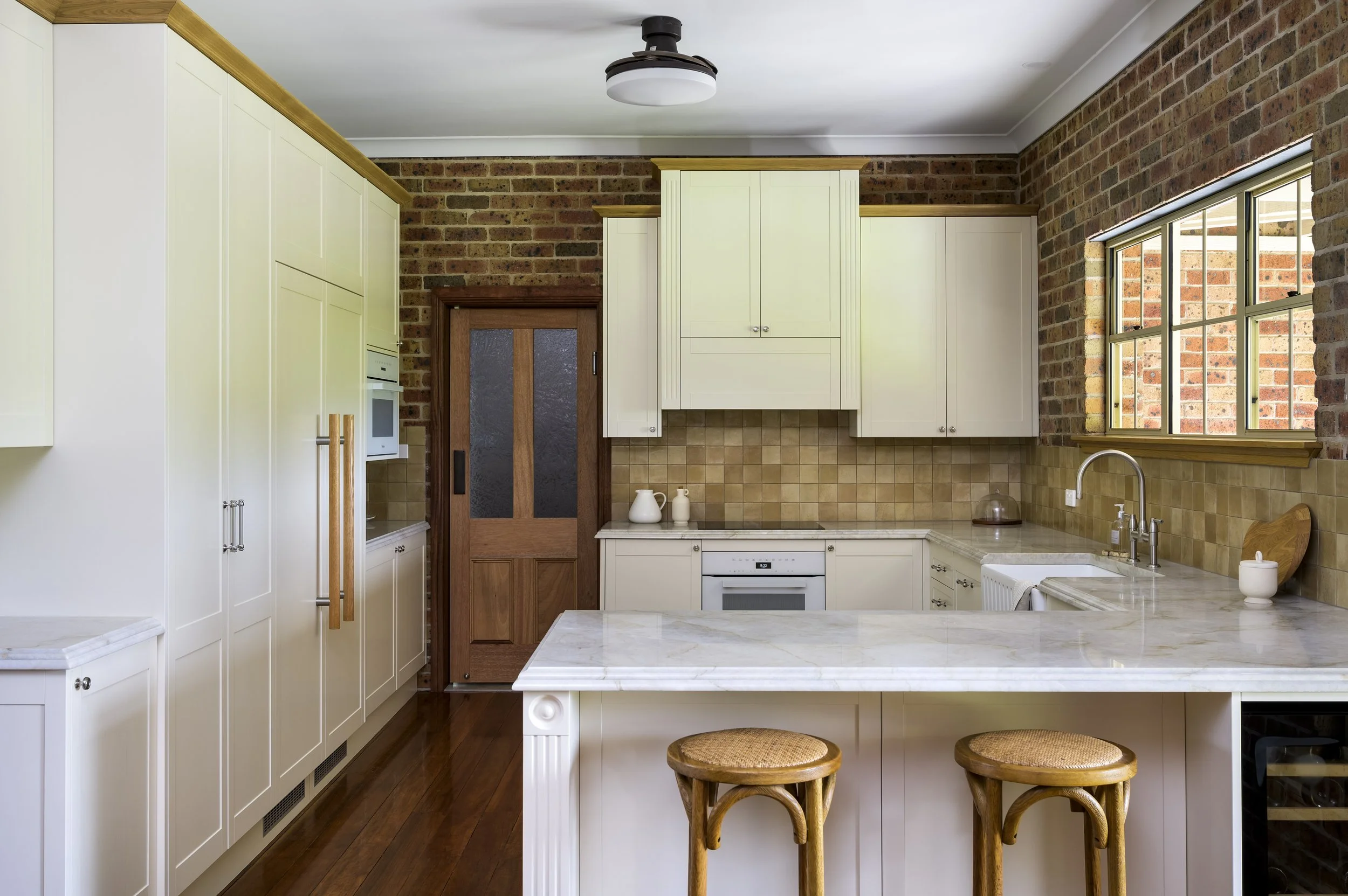 Kitchen with cream cabinets, brick walls, and a marble countertop island with two wooden stools.