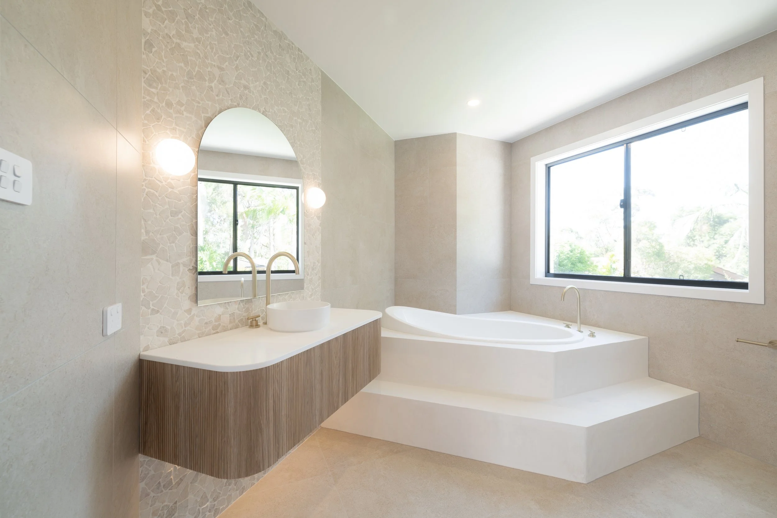 Modern bathroom with a large window, a built-in bathtub, and a floating vanity with an oval mirror and vessel sink.