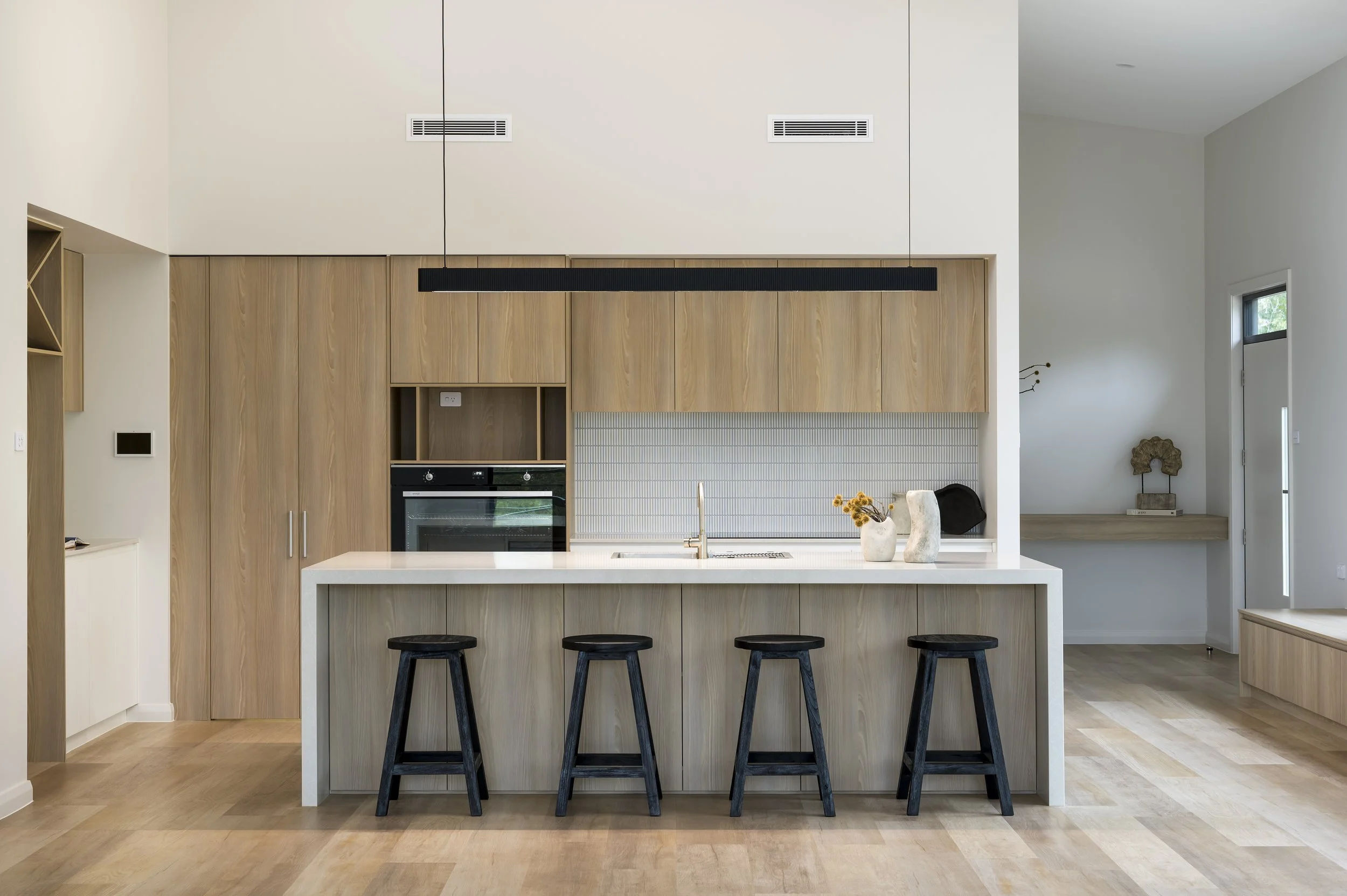 Modern kitchen with light wood cabinets, white island, four black stools, and minimal decor.