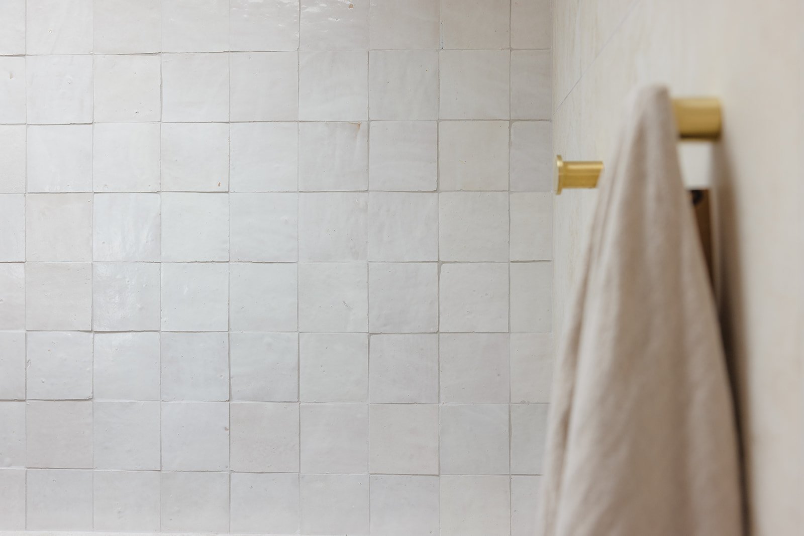 Close-up of a beige towel hanging on a wall-mounted gold towel rack in a tiled bathroom.