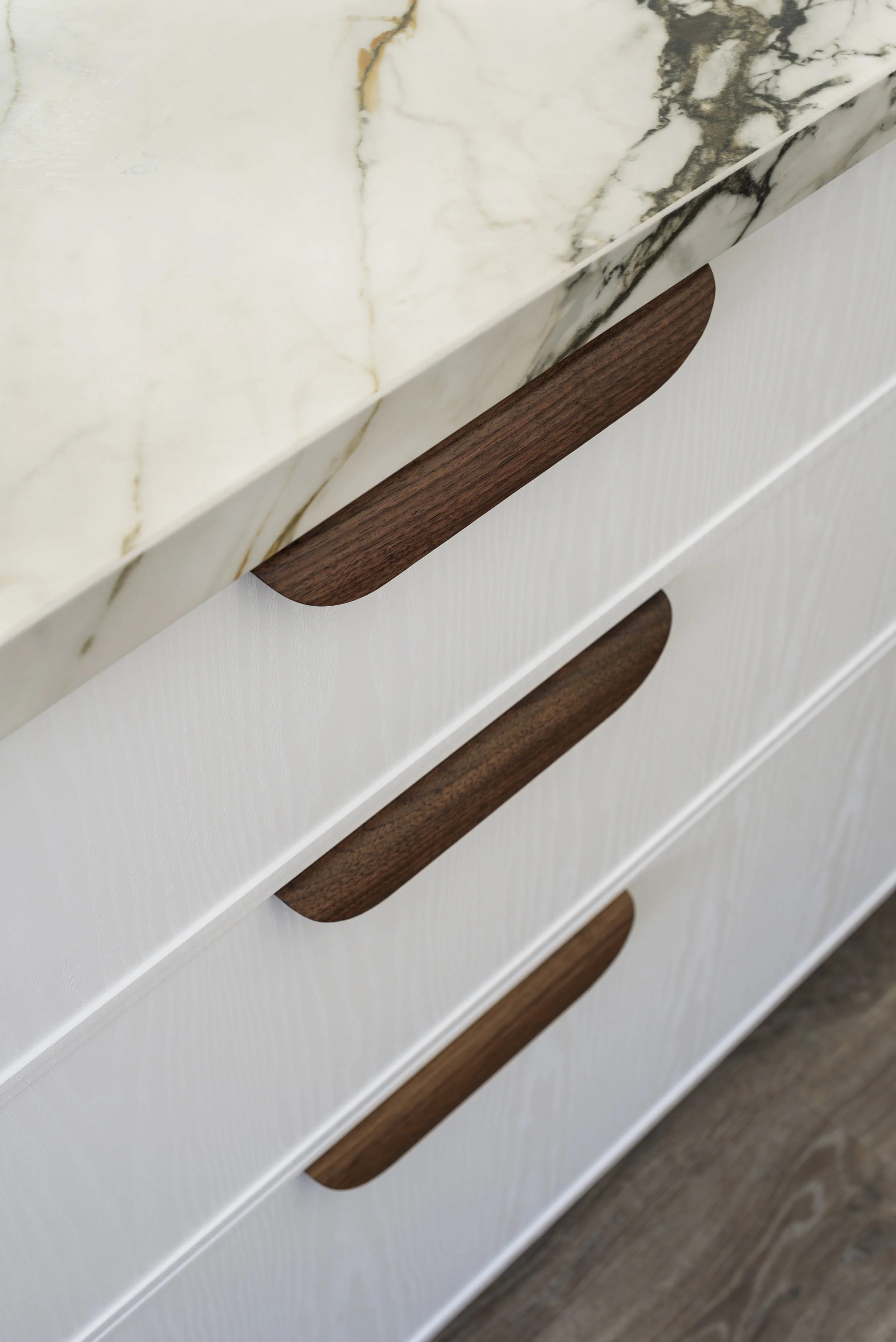 Close-up of a white dresser with dark wooden handles and a marble top.