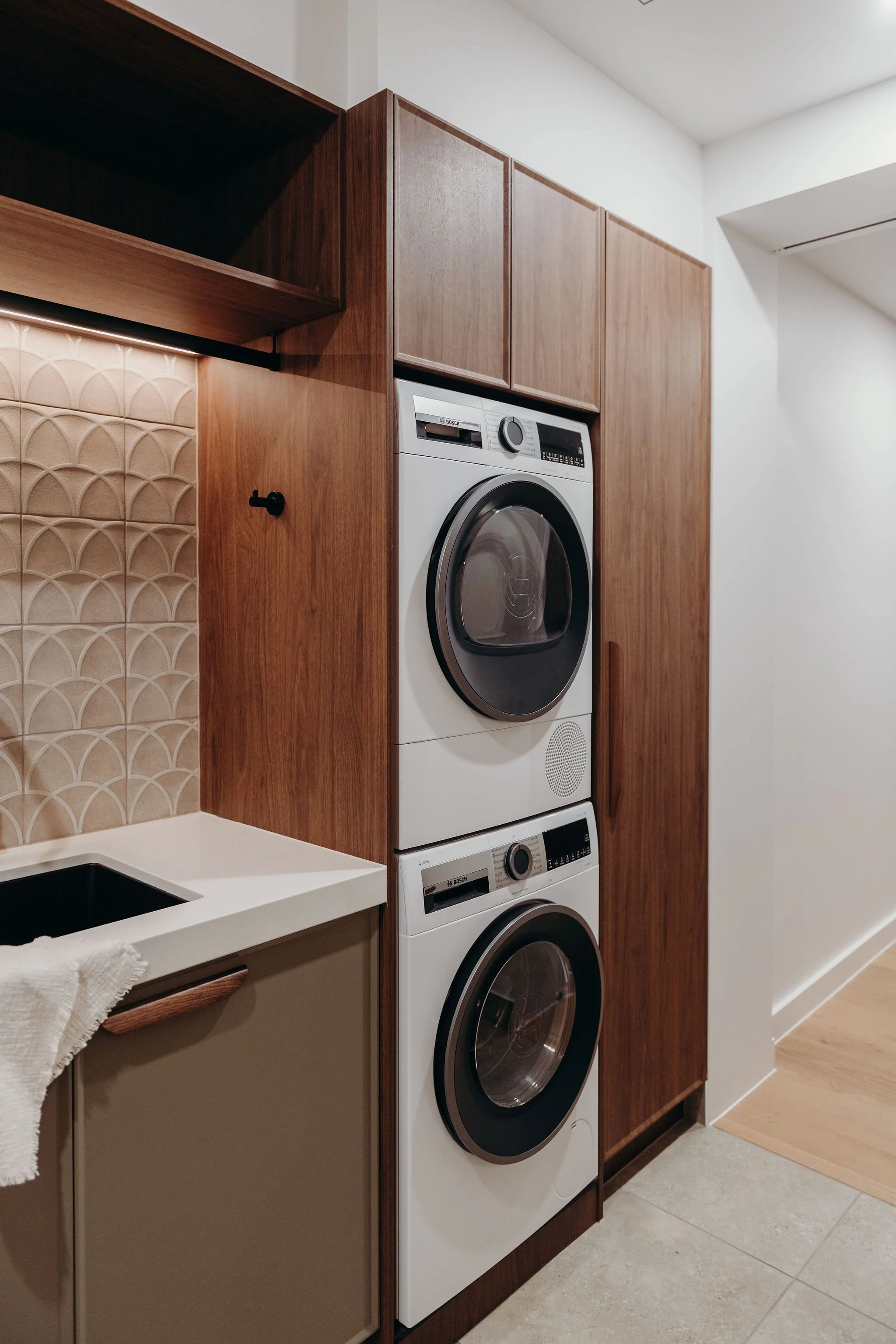 Stacked white washer and dryer in a laundry room with wooden cabinets and a tiled backsplash.