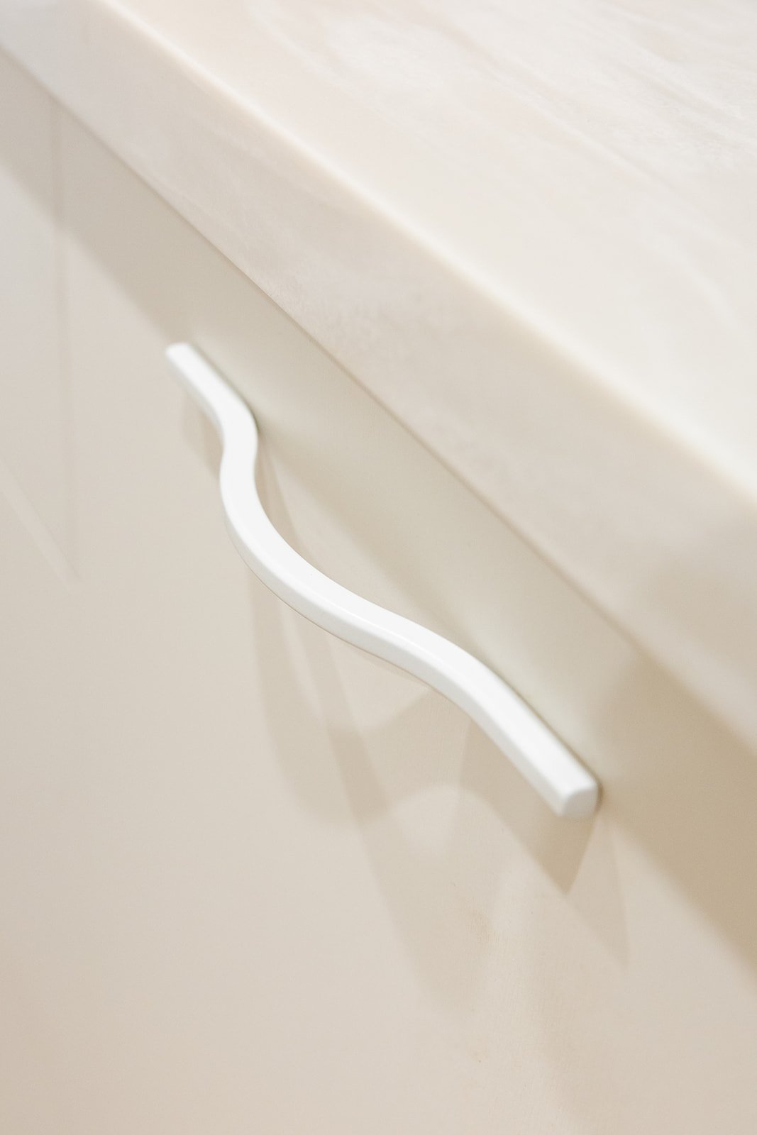 Close-up of a white, curved cabinet handle on a cream-colored cabinet drawer.