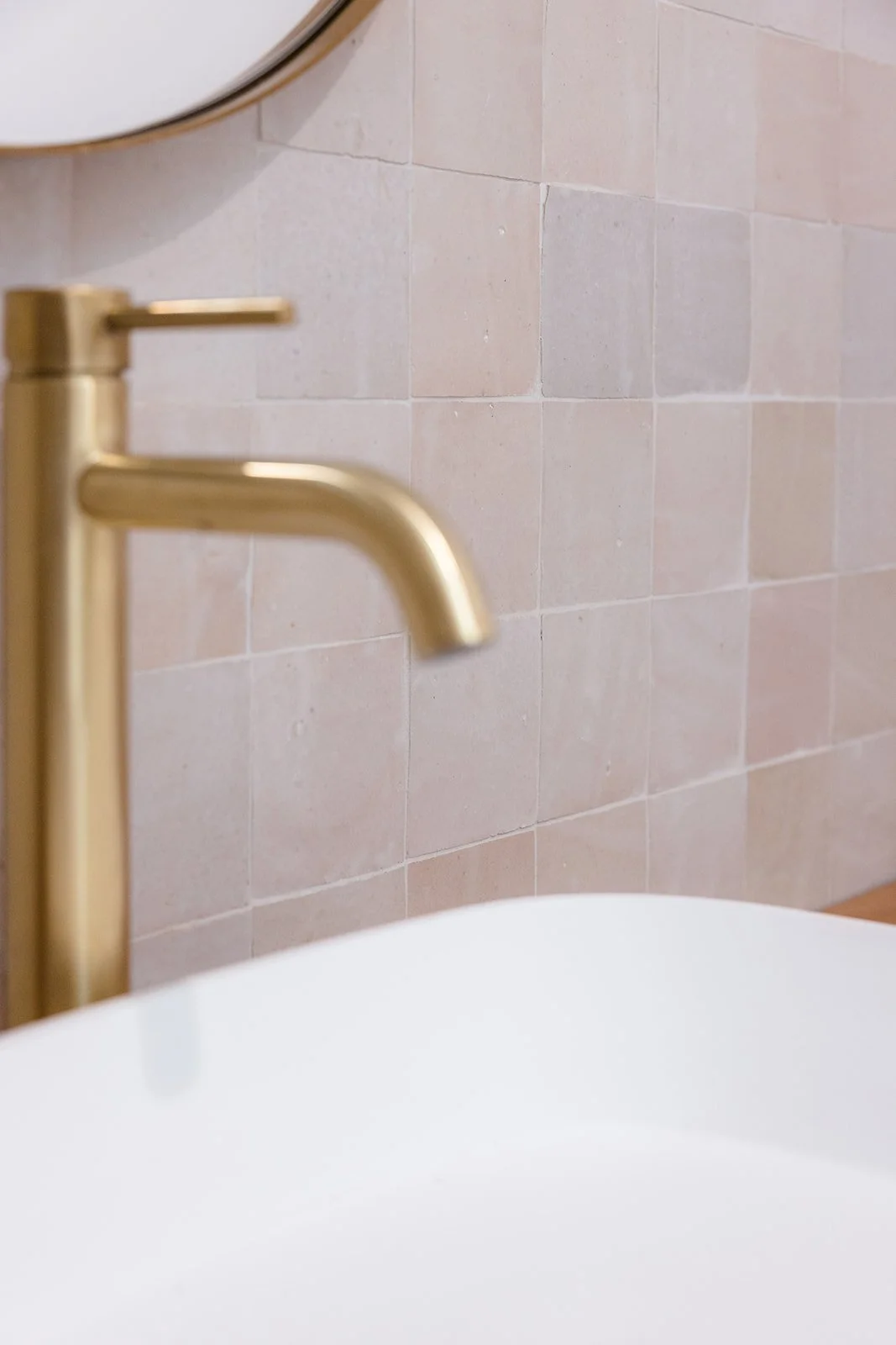 Close-up of a gold faucet mounted on a tiled bathroom wall with a vessel sink below.