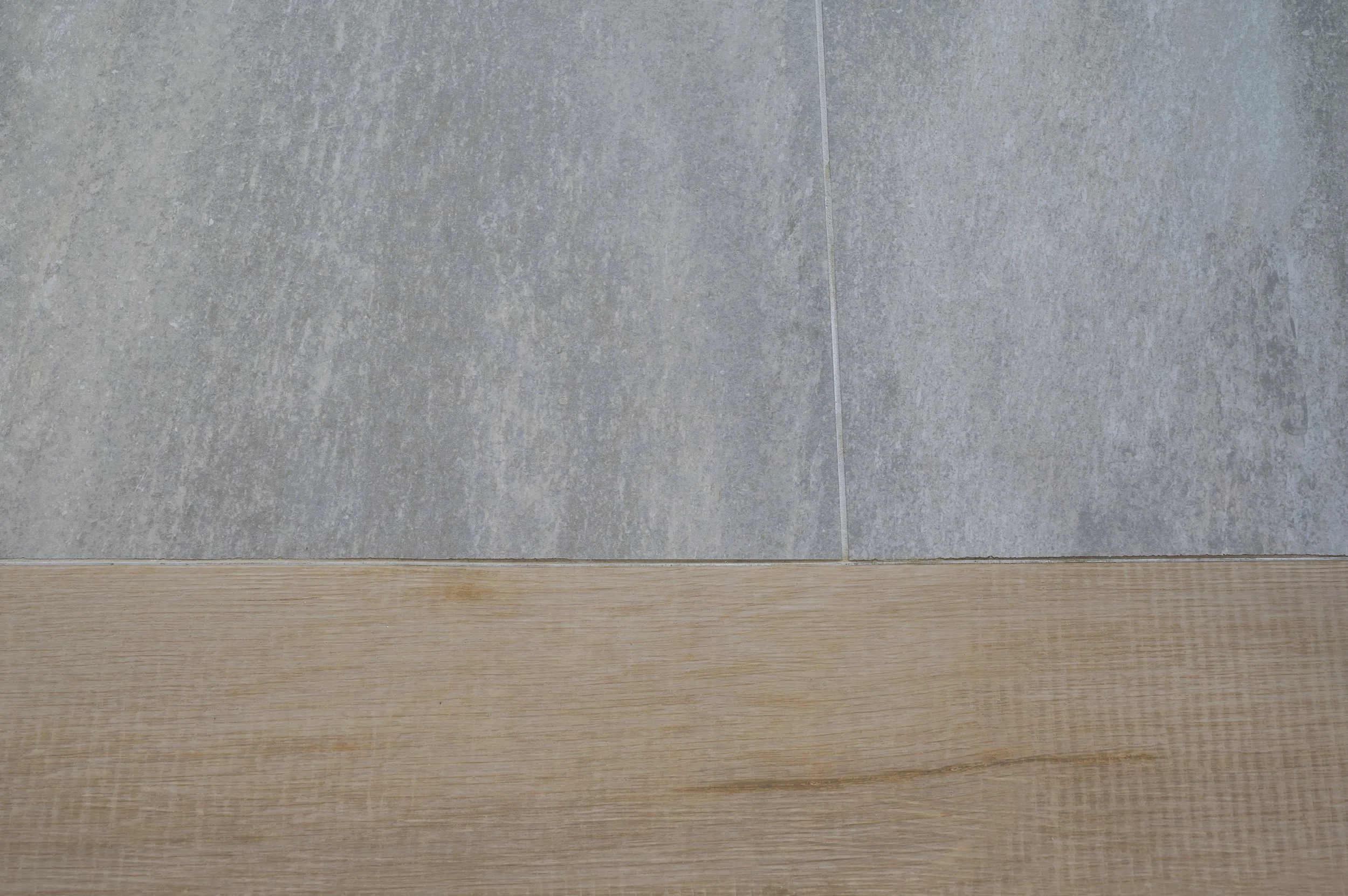 Close-up of a corner where a wooden floor meets a tiled wall.