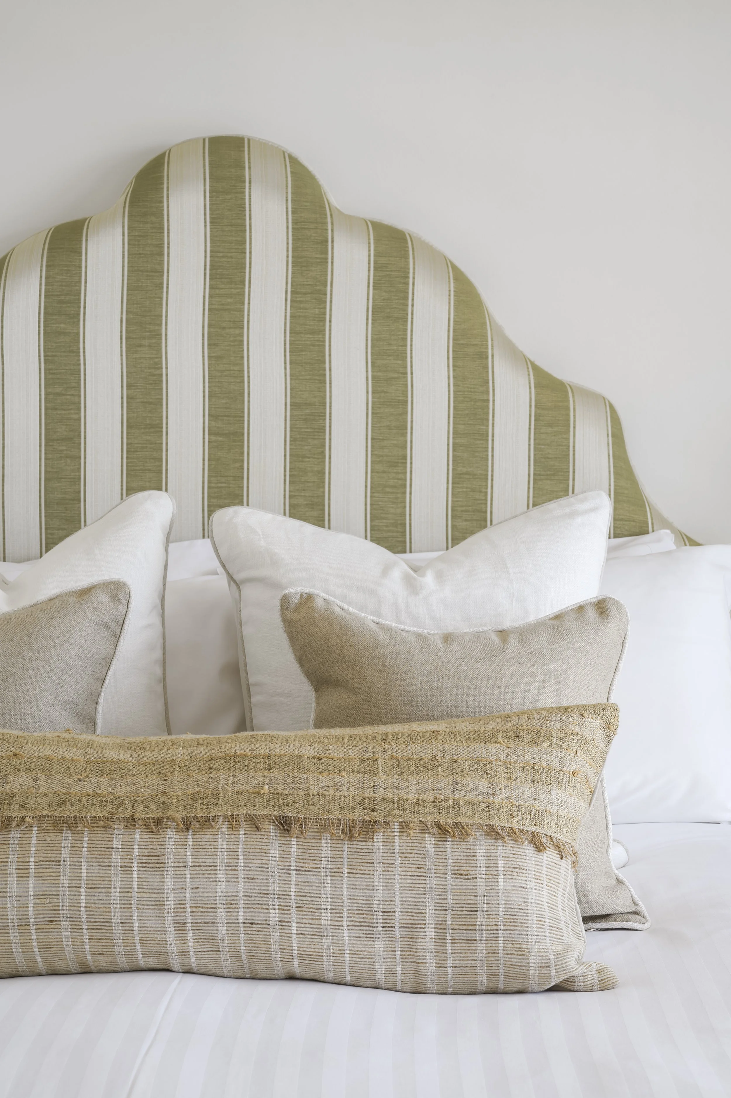 A bed with multiple pillows and an upholstered headboard with green and white stripes.