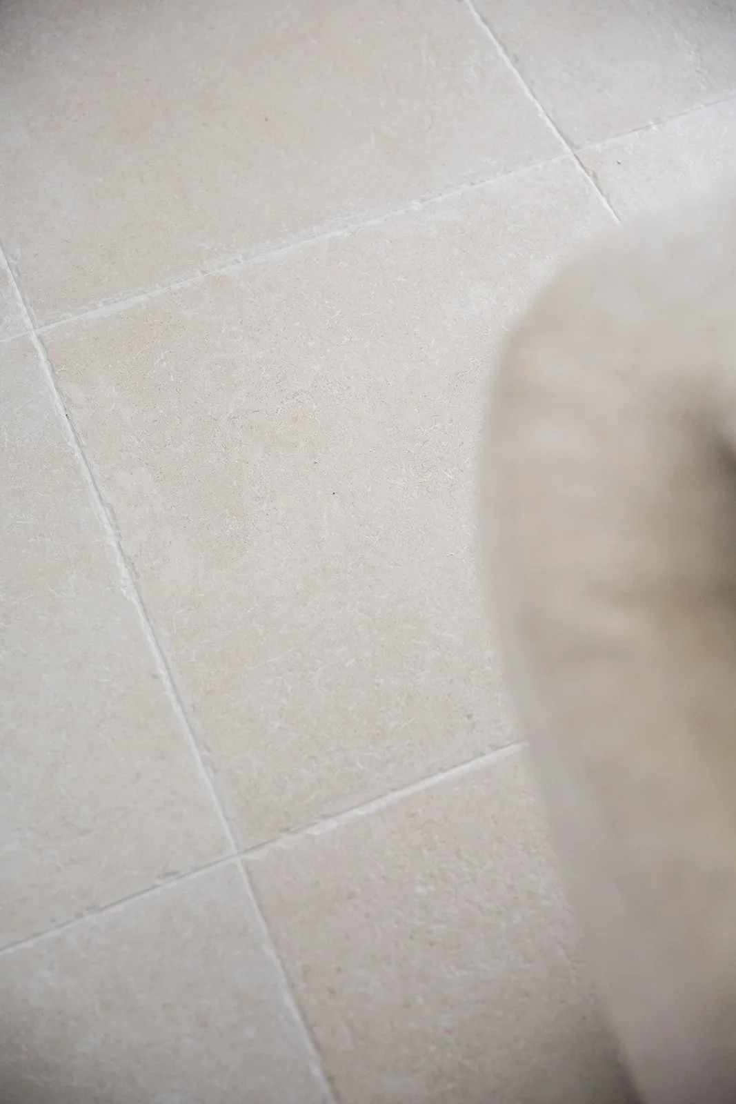 Close-up of beige tiled floor with grout lines and part of a blurred object on the right side.