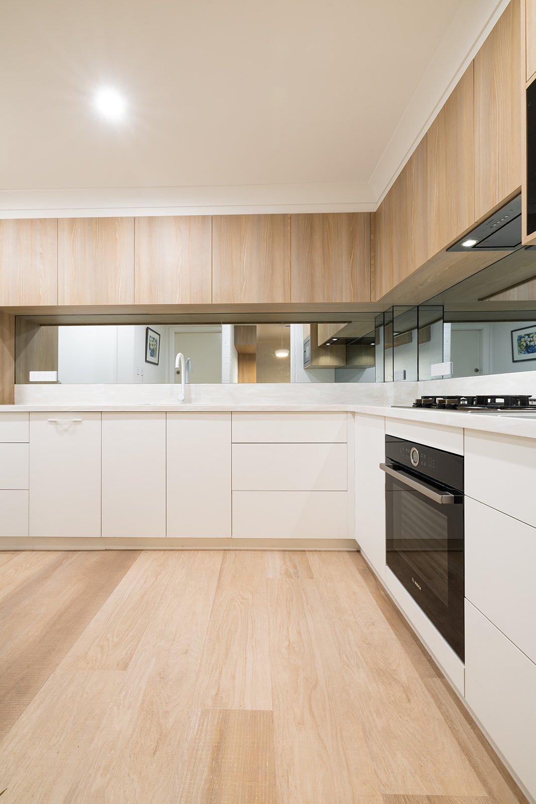 Modern kitchen with white cabinets, light wood flooring and wall paneling, and a built-in oven.