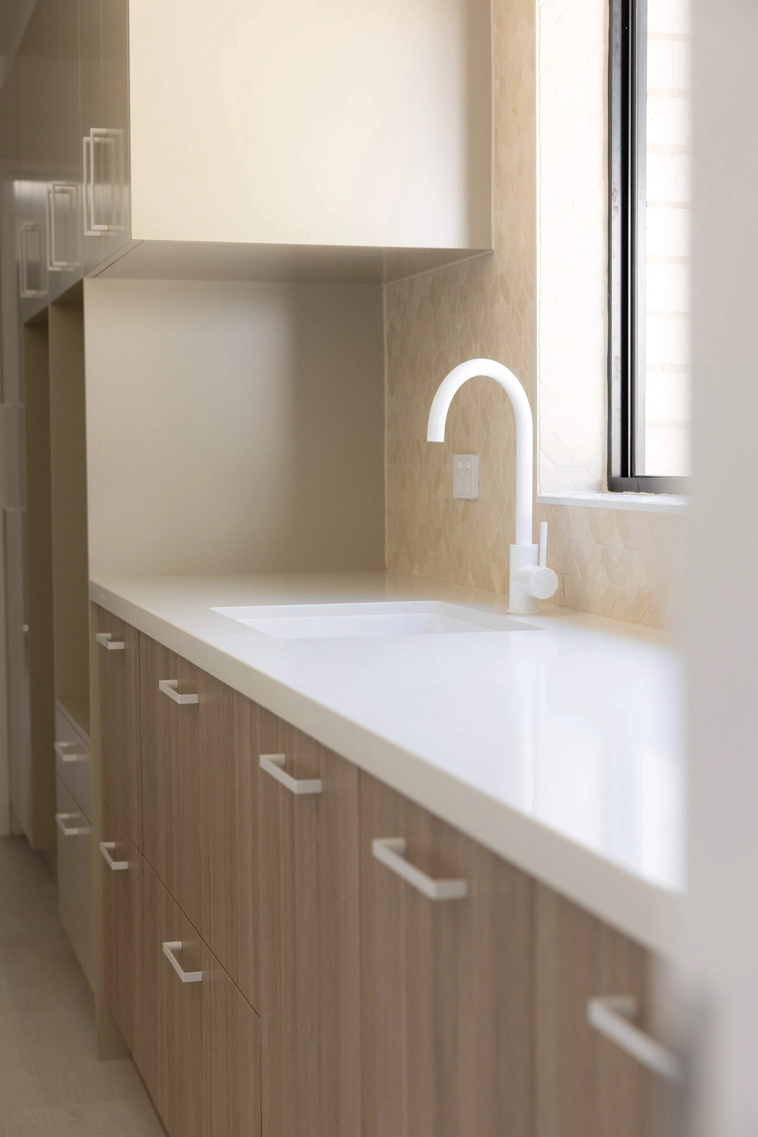 Bright modern kitchen with white countertop, white sink, and white faucet near a window with natural light.
