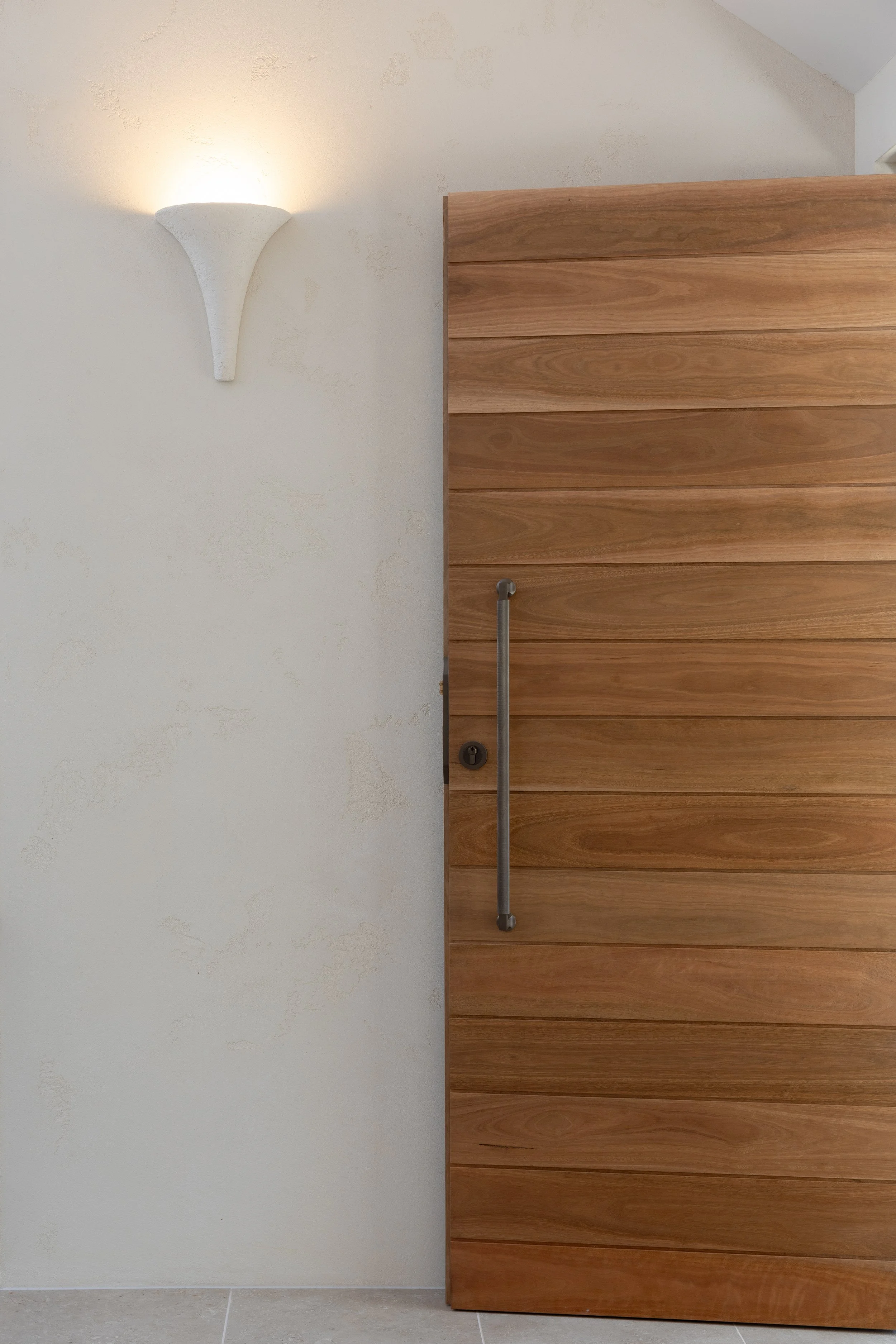 Wooden door with metal handle, light wall with textured finish, and a wall sconce light fixture.