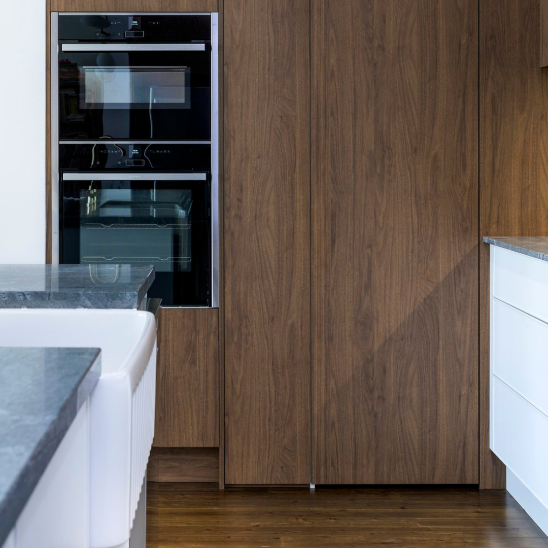 Kitchen with built-in black oven and microwave, wooden cabinetry, gray countertop, white cabinetry on the right, and hardwood flooring.