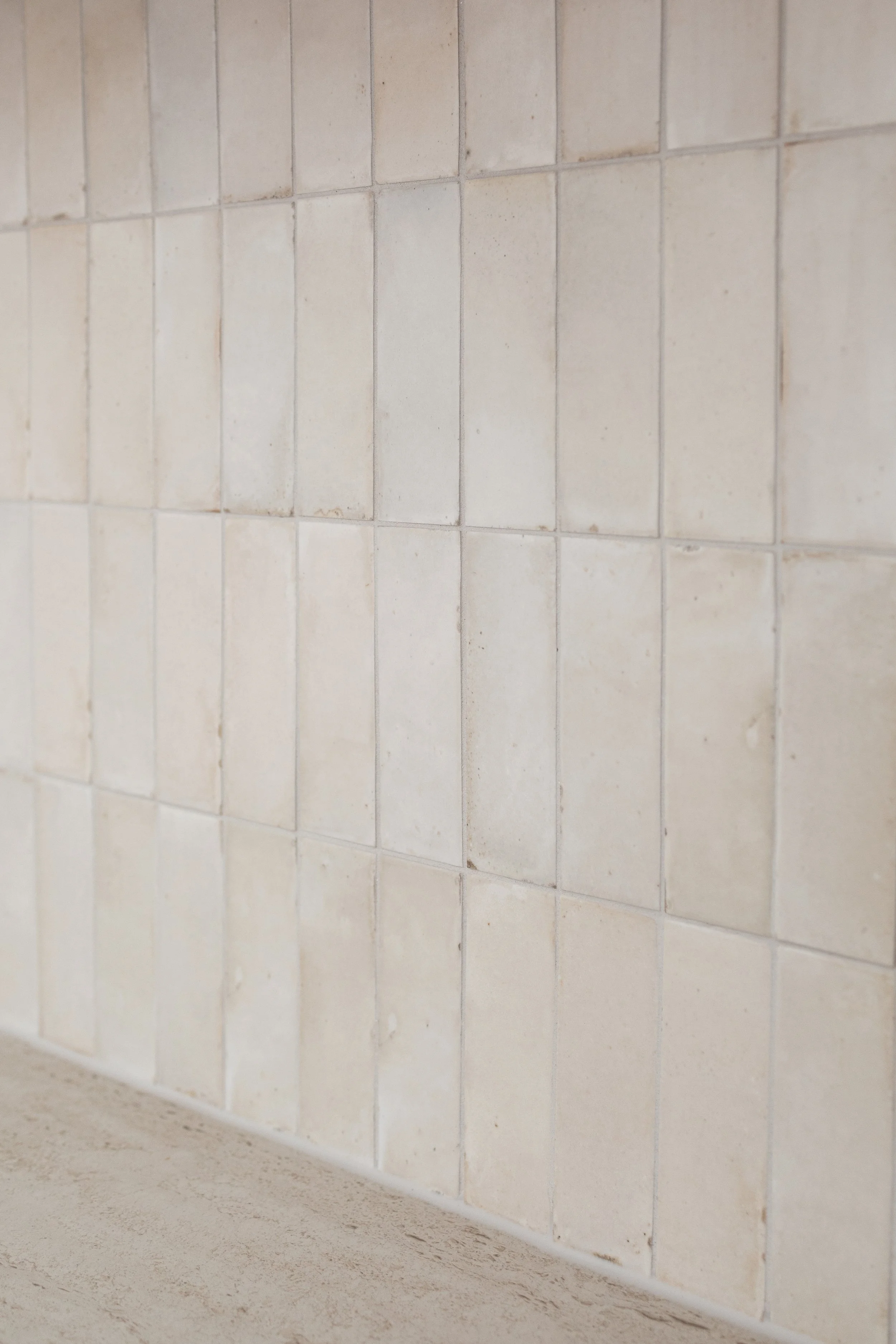 Close-up view of a tiled wall with off-white square tiles and a beige floor.
