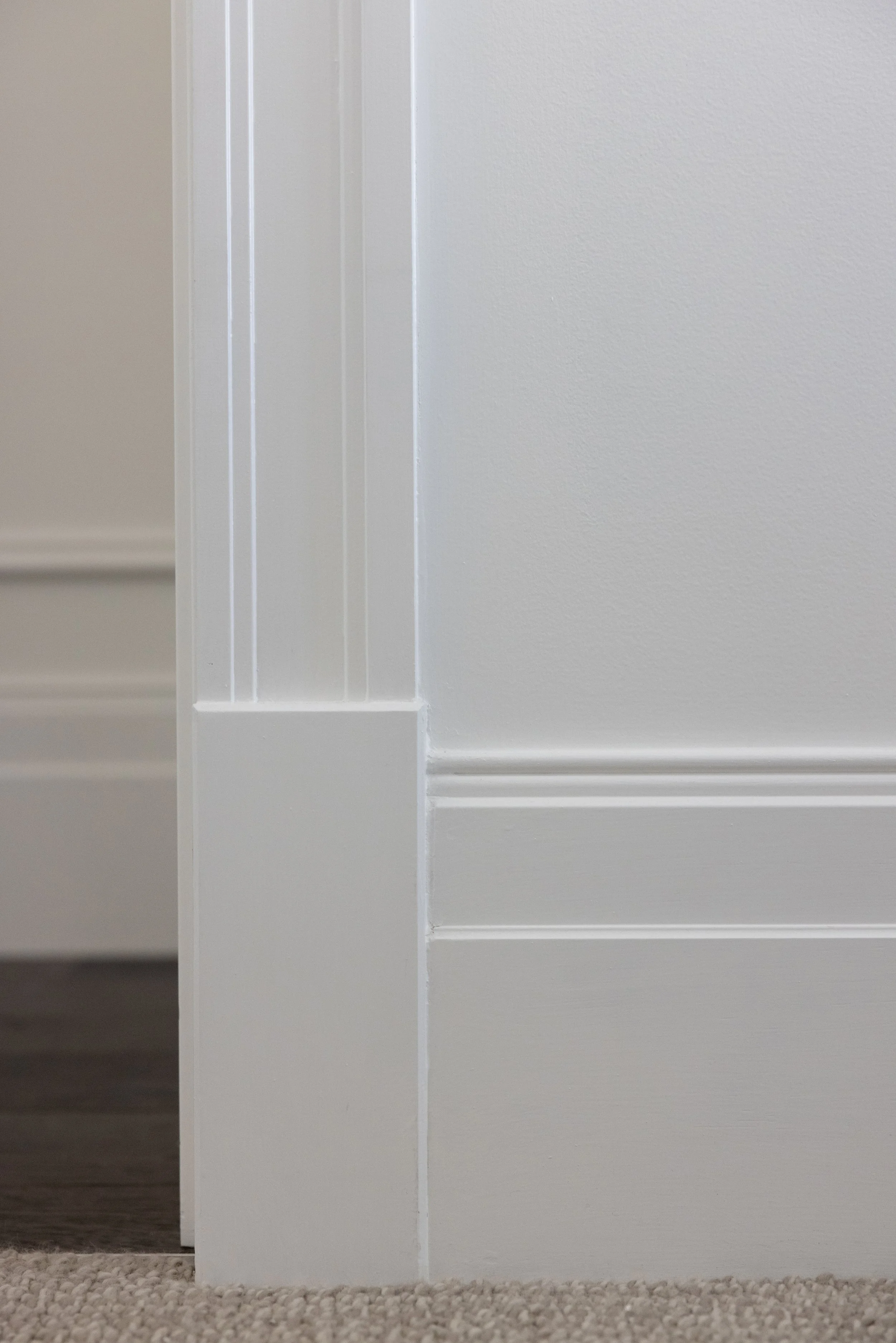 Close-up of a white doorframe and wall with detailed molding, next to a carpeted floor.