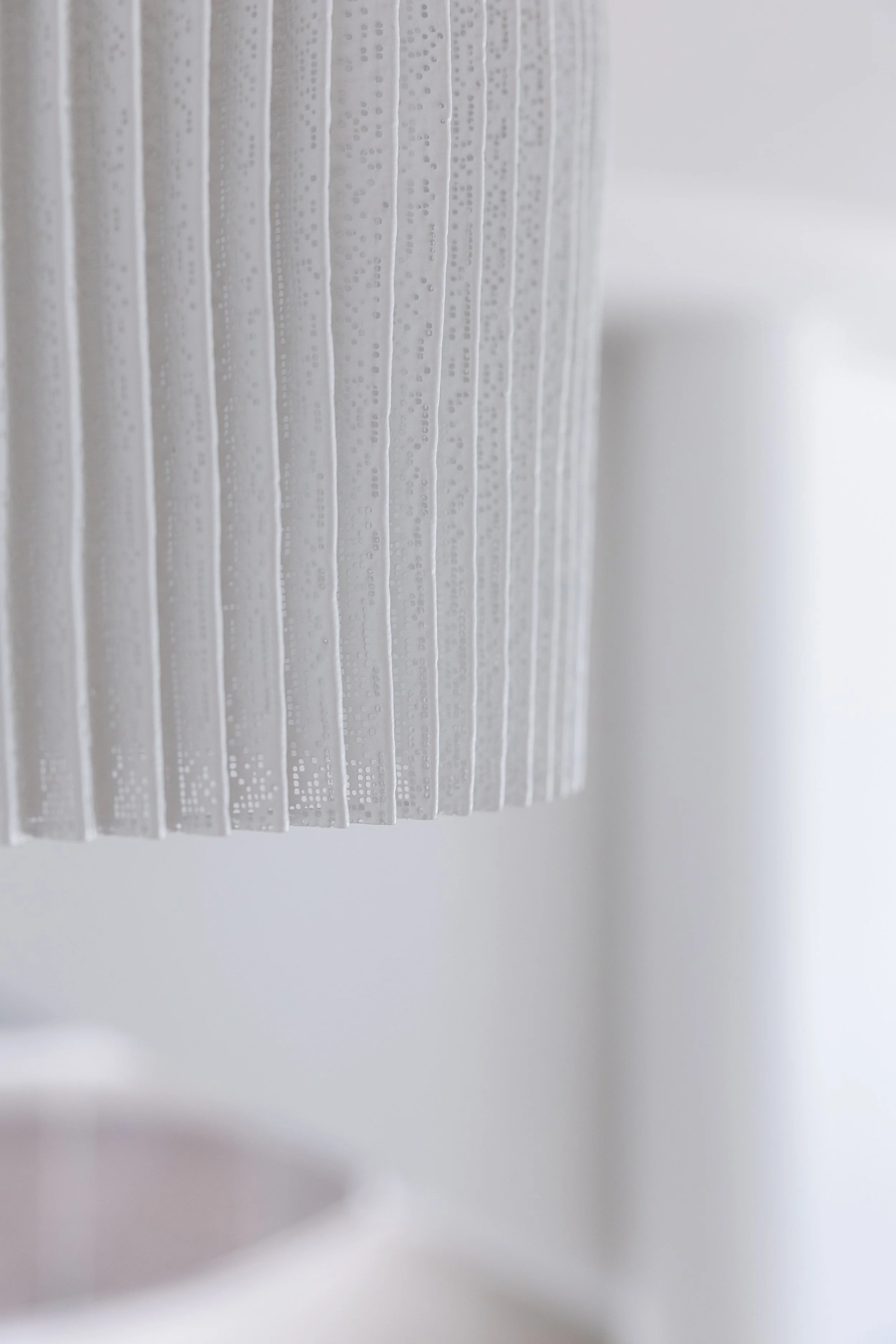 Close-up of a white textured lampshade with vertical ridges and small perforations.
