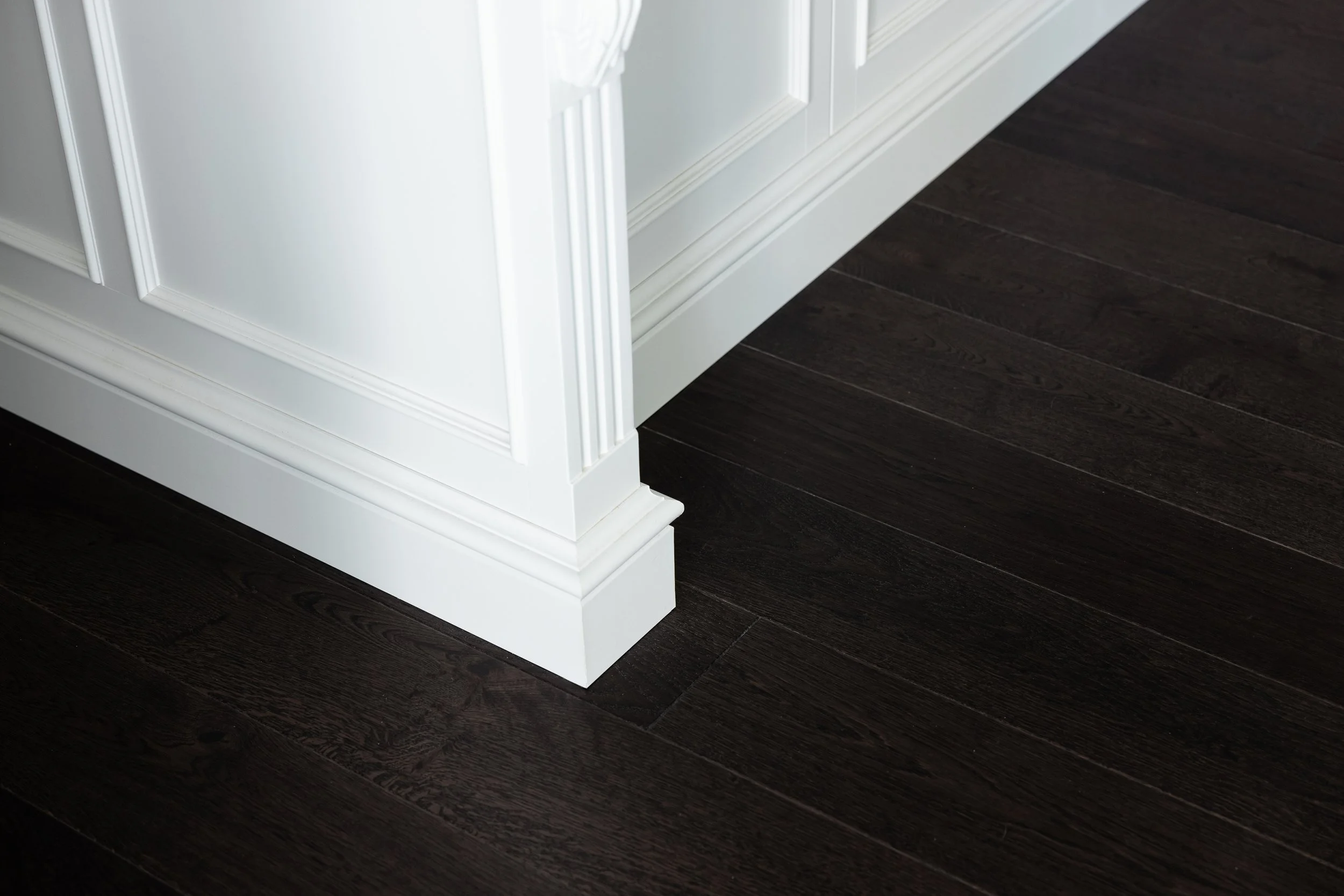 Corner of a white cabinet or furniture piece with decorative molding, positioned on a dark hardwood floor.