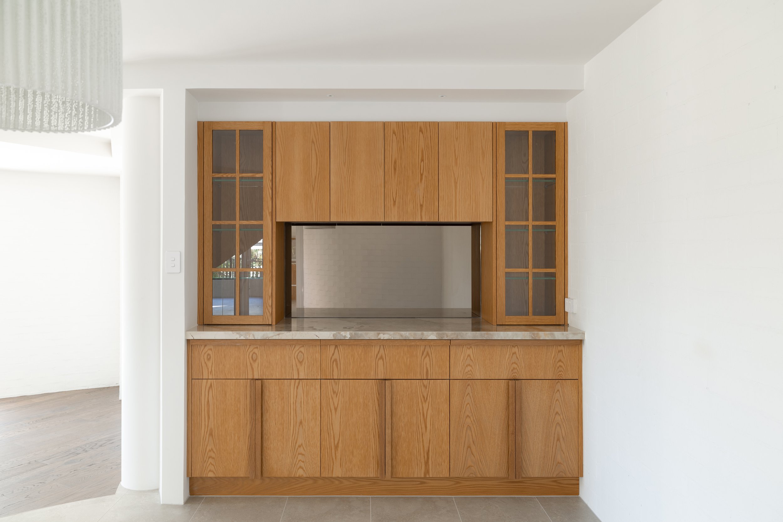 Wooden built-in kitchen cabinet with glass-paneled doors and marble countertop.