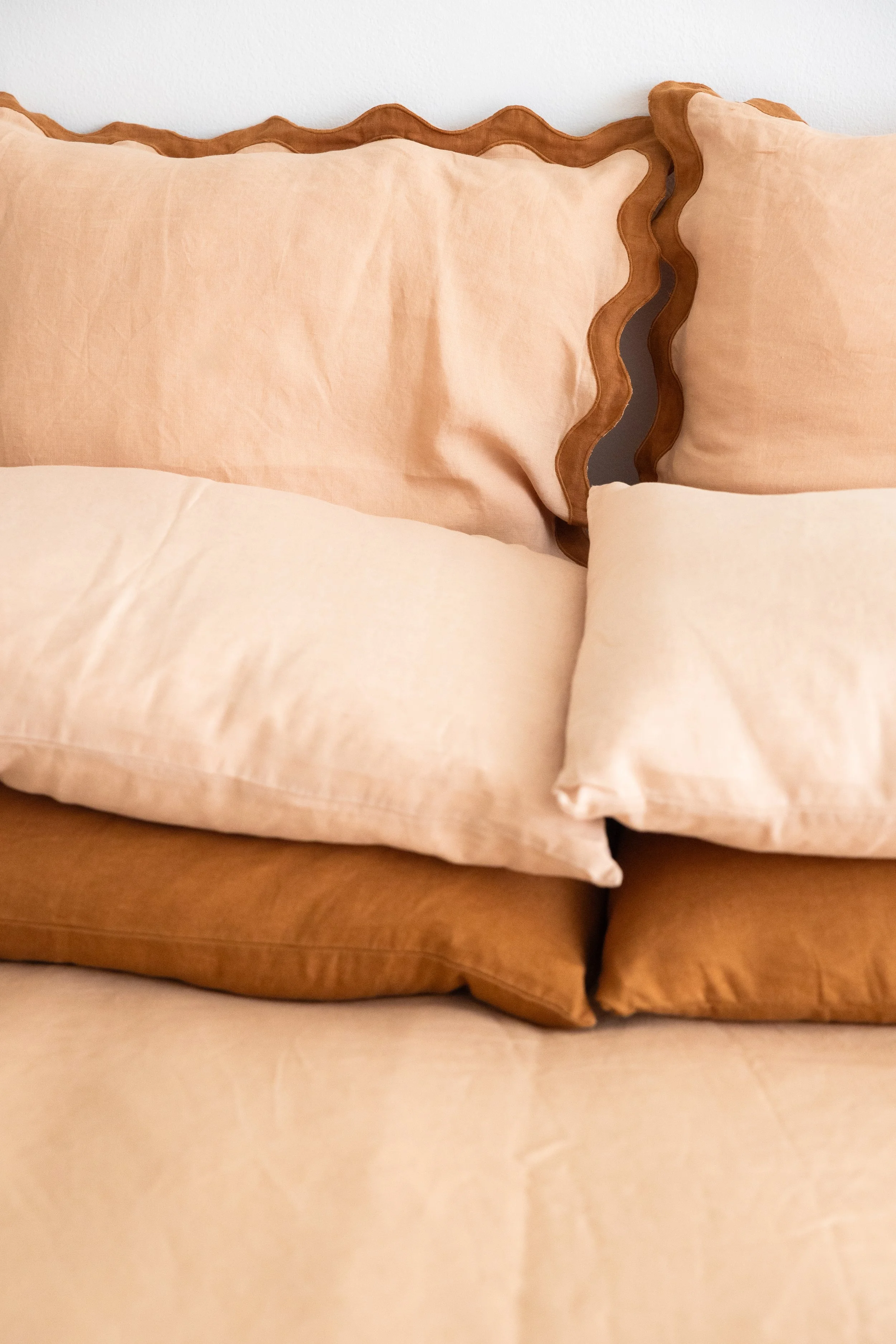 Stacked peach, light brown, and darker brown pillows on a bed.