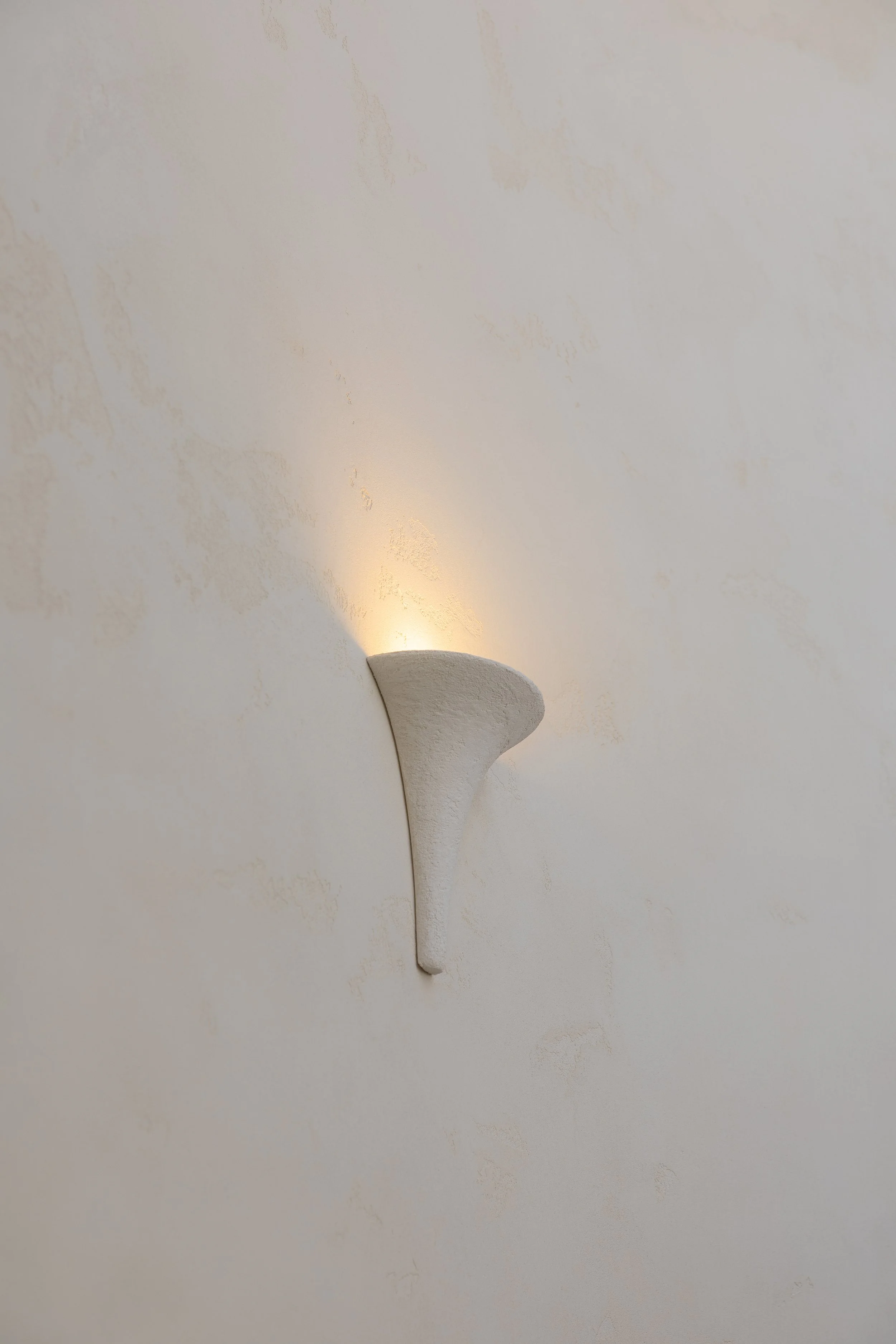 Modern wall sconce with a textured white surface, emitting warm light onto a lightly textured white wall.