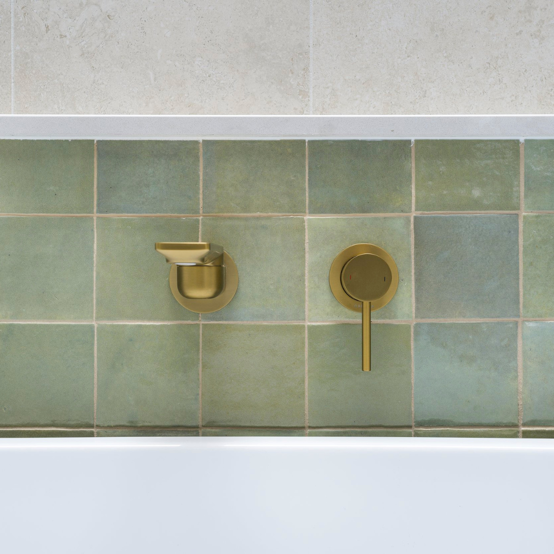 Close-up of a green tiled bathroom wall with gold faucet and handle, above a bathtub.