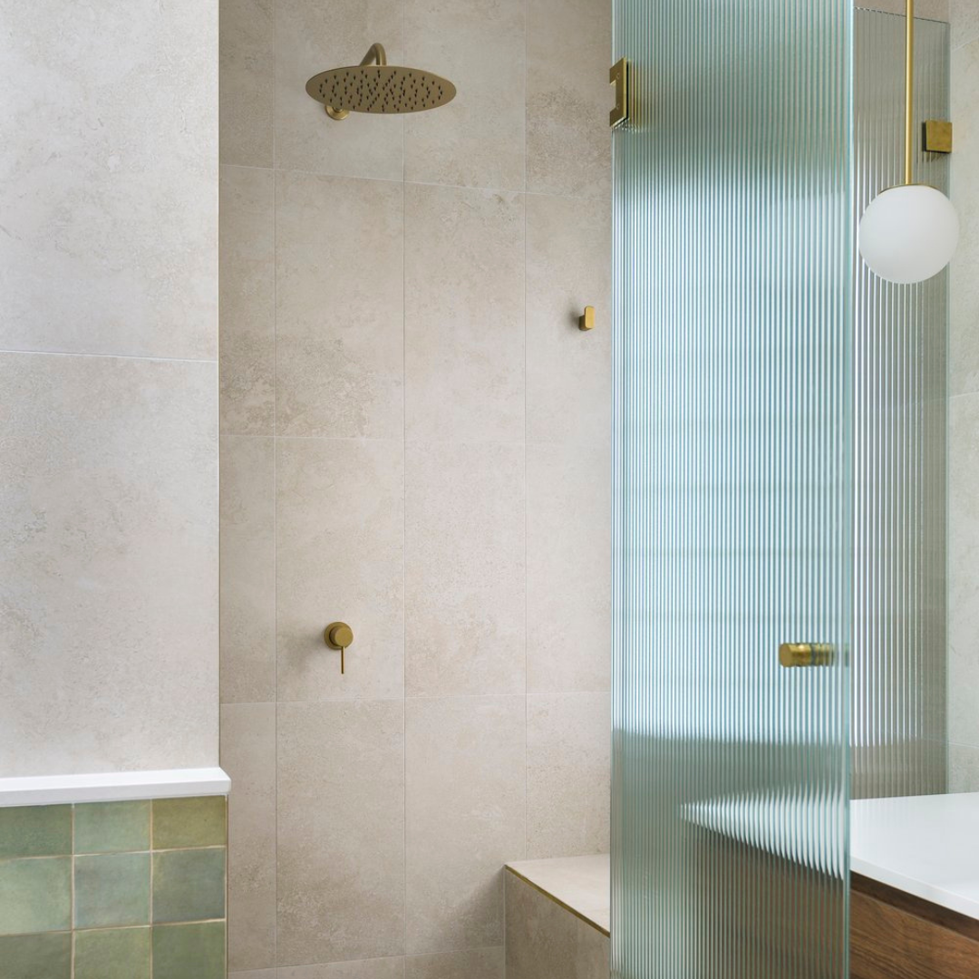 Modern bathroom shower area with round rain shower head, textured glass partition, and beige tiled walls.