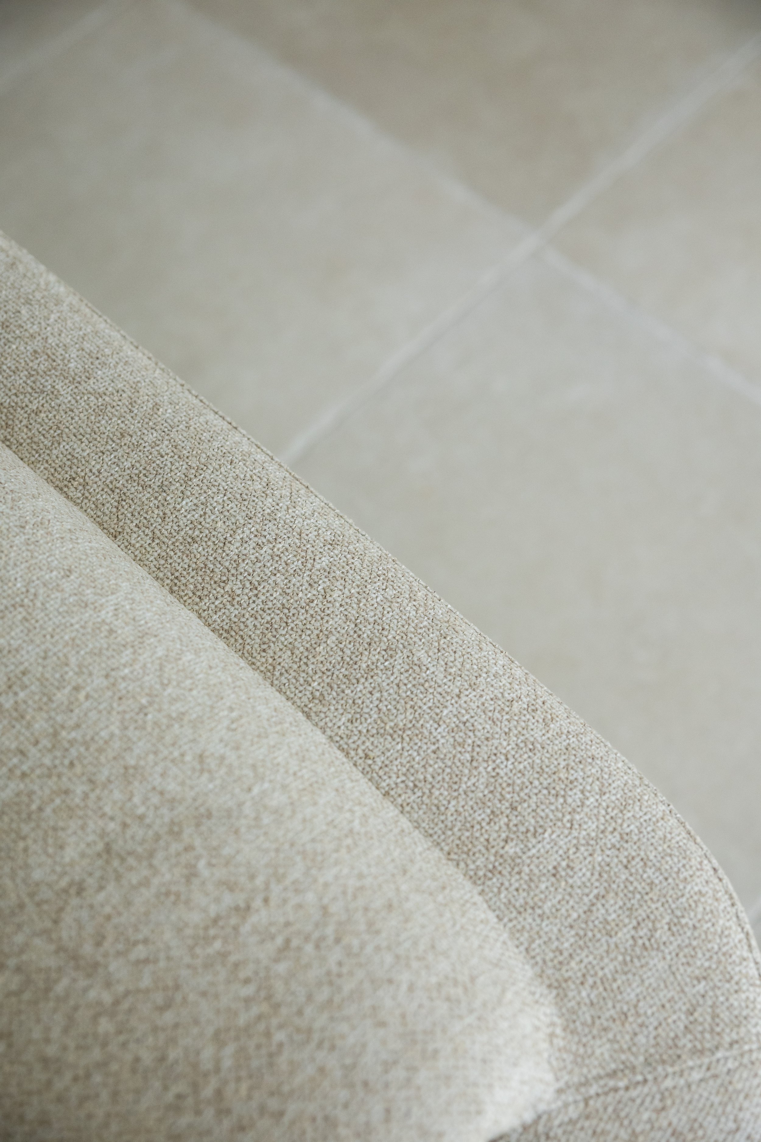 Close-up of a beige fabric armrest and light-colored tile floor.
