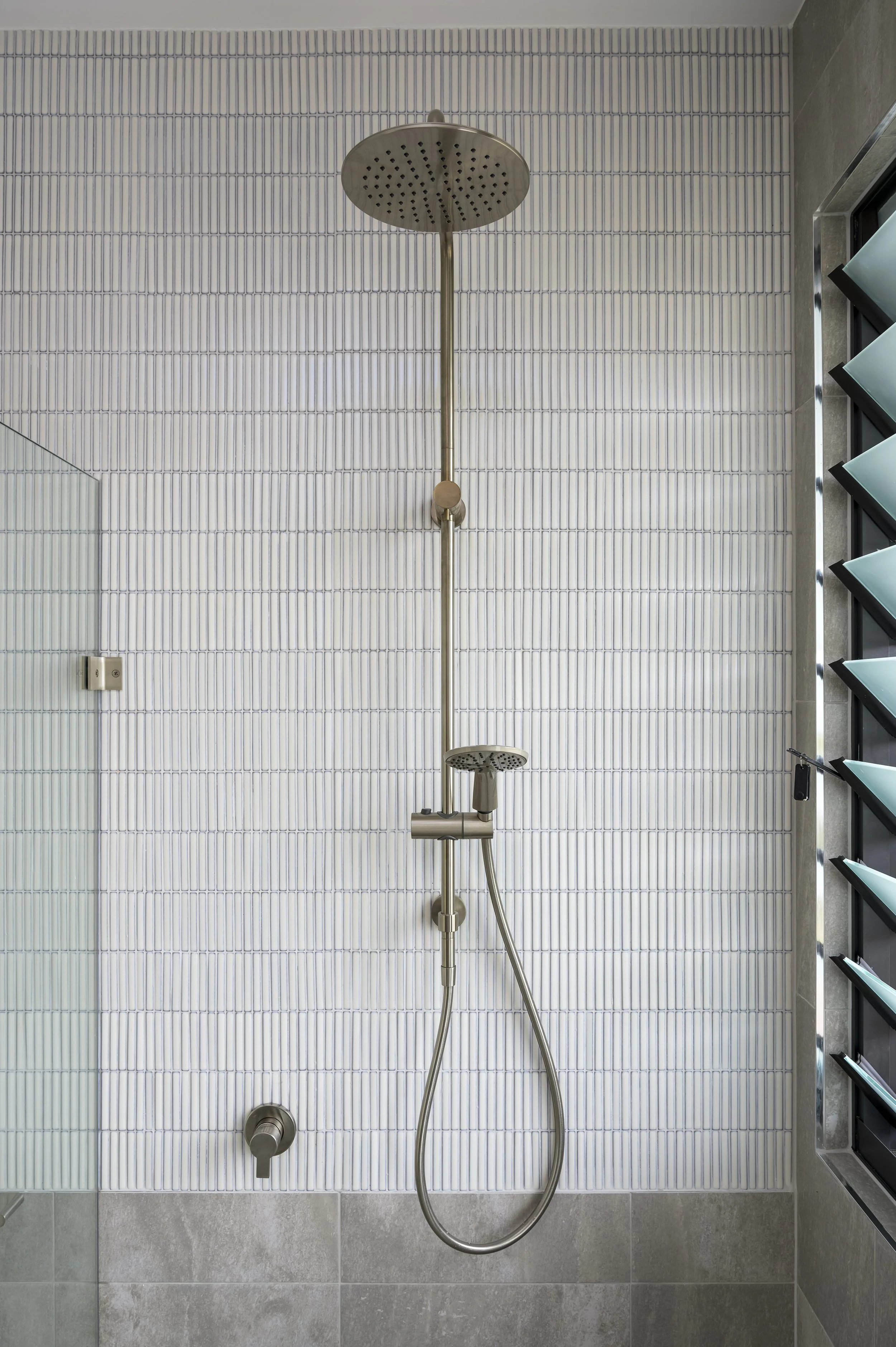 Modern shower with a round overhead rain showerhead, a handheld showerhead, and a tiled wall in a bathroom.