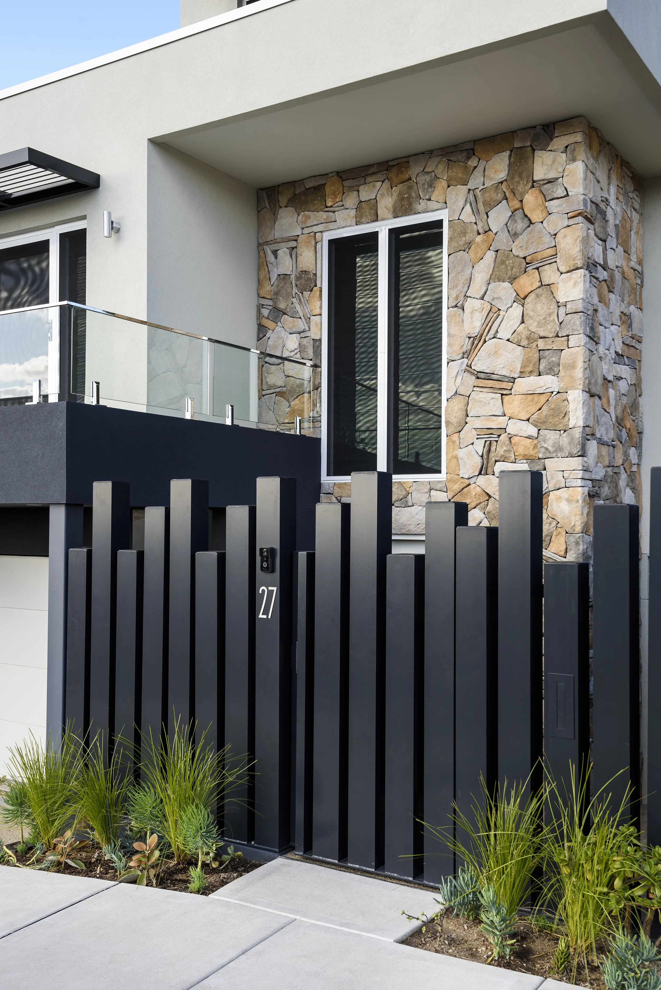 Modern house with stone accent wall, black gate with house number 27, and small plants in front.