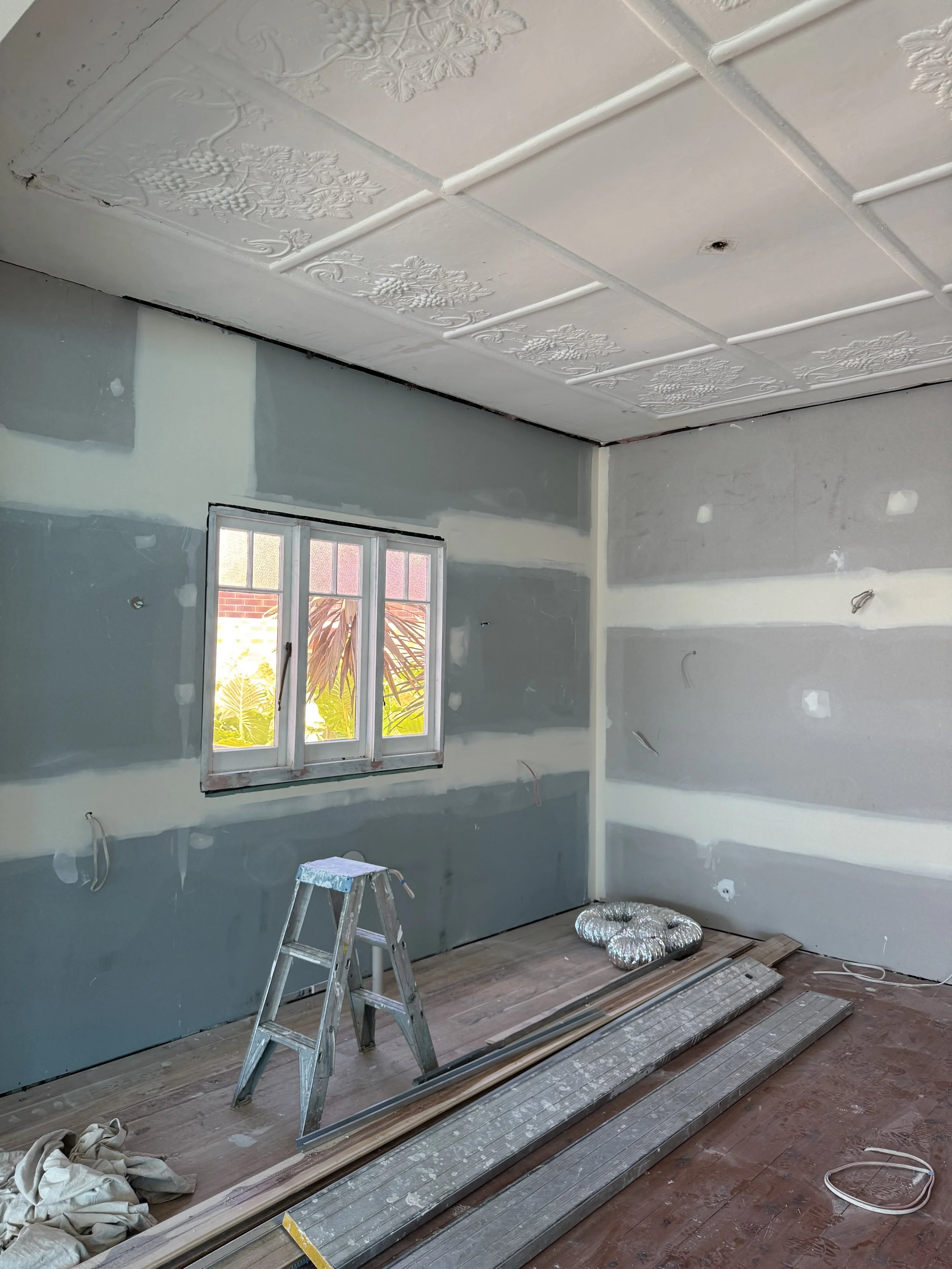 Room under construction with drywall, window, ladder, and building tools on the floor.