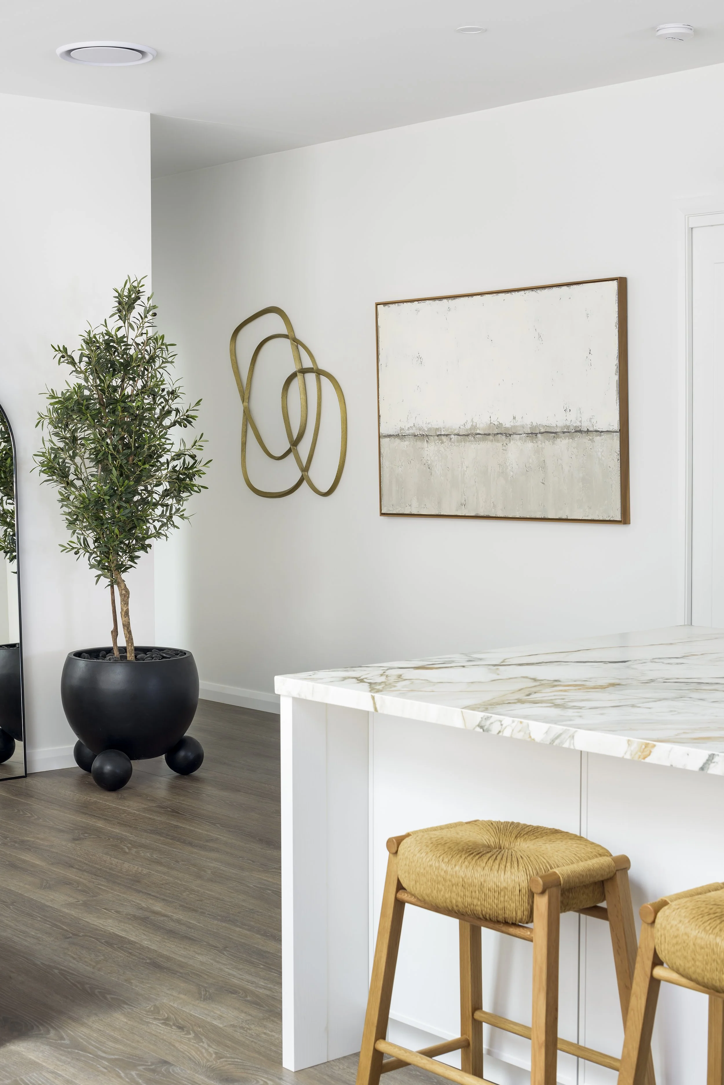 Modern interior with a tall potted tree, wall art, marble countertop, and yellow upholstered barstools.