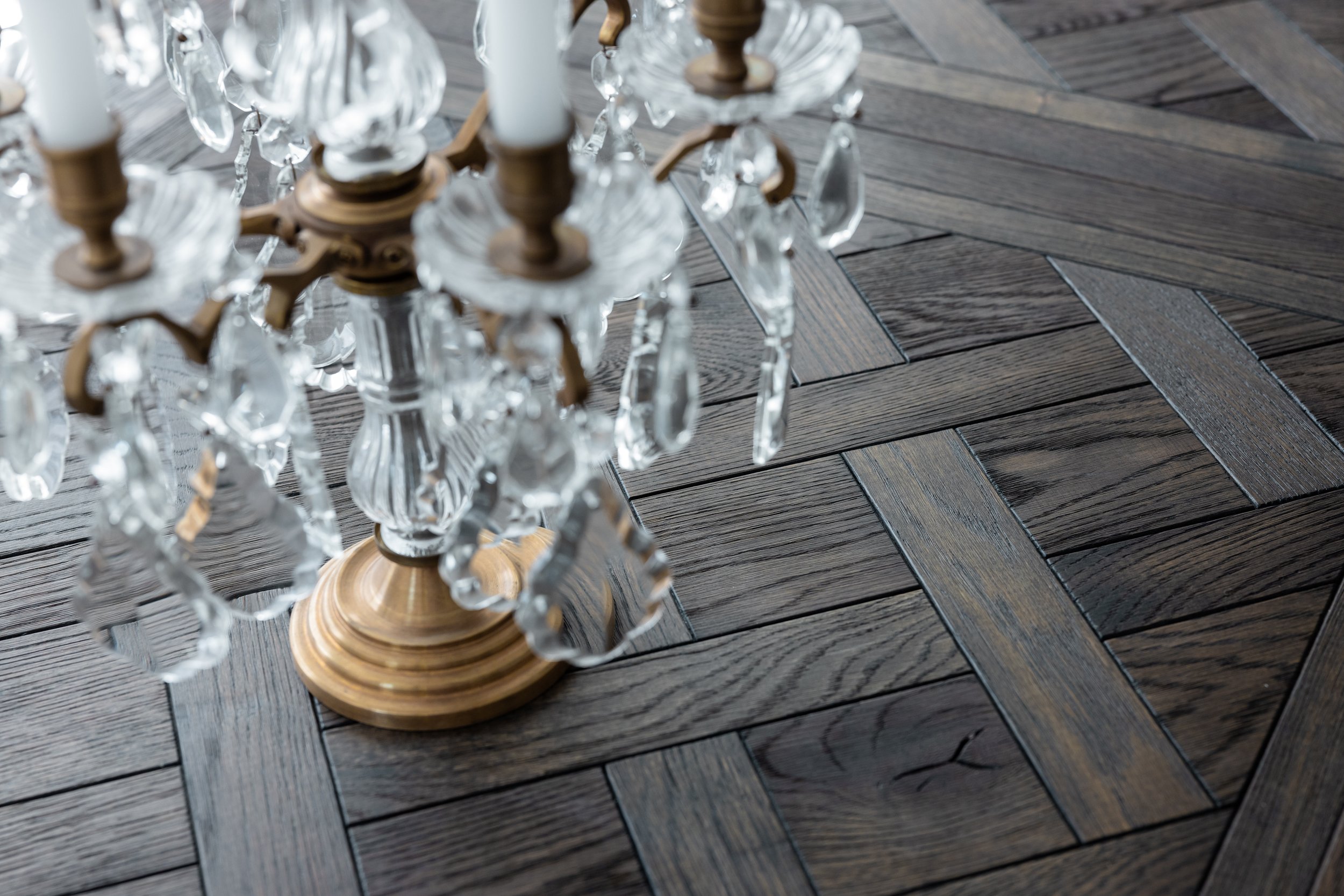 Close-up of a crystal chandelier with a wooden base, hanging over a dark wood parquet floor.
