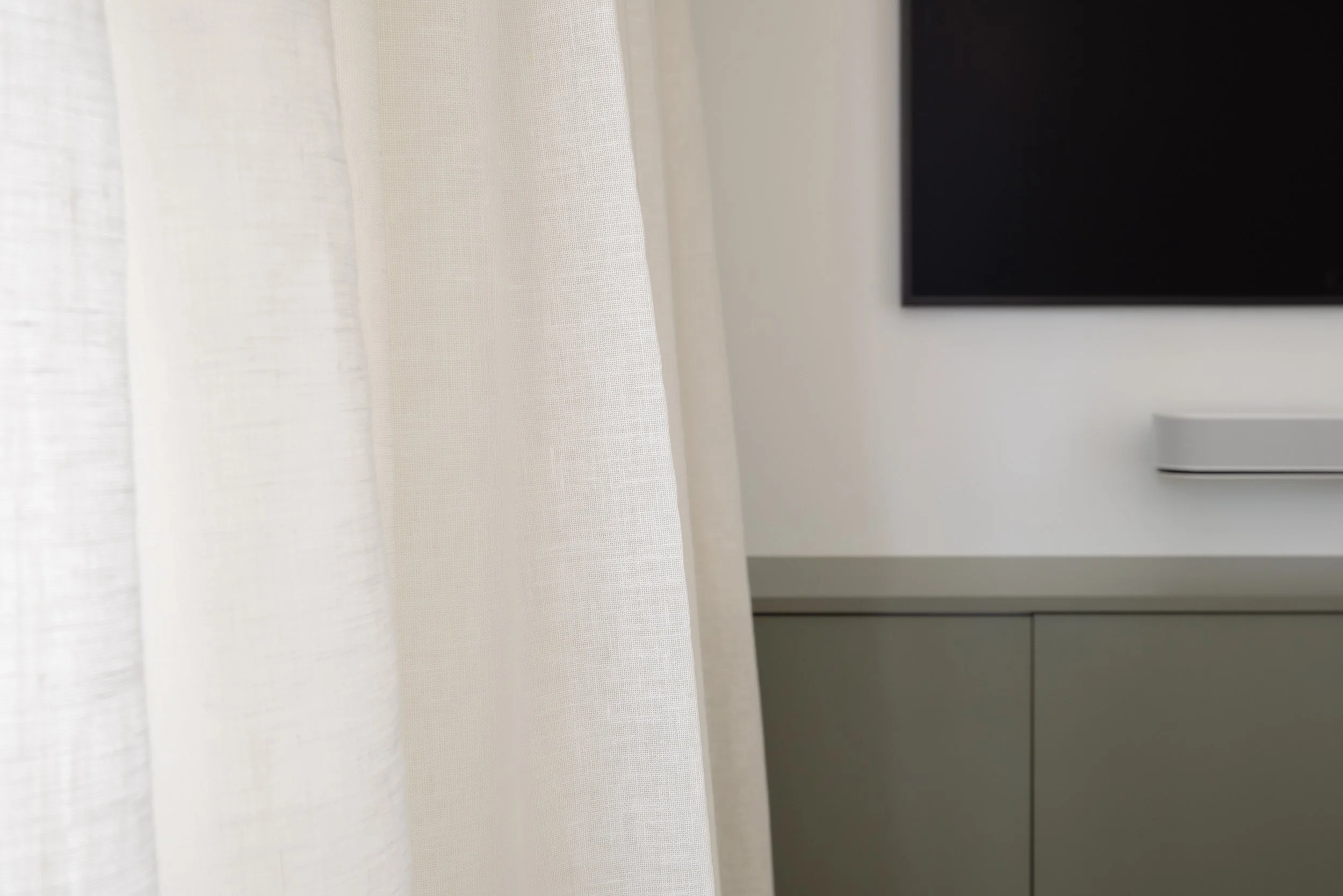 Close-up of sheer white curtains with a gray cabinet and a black television in the background.