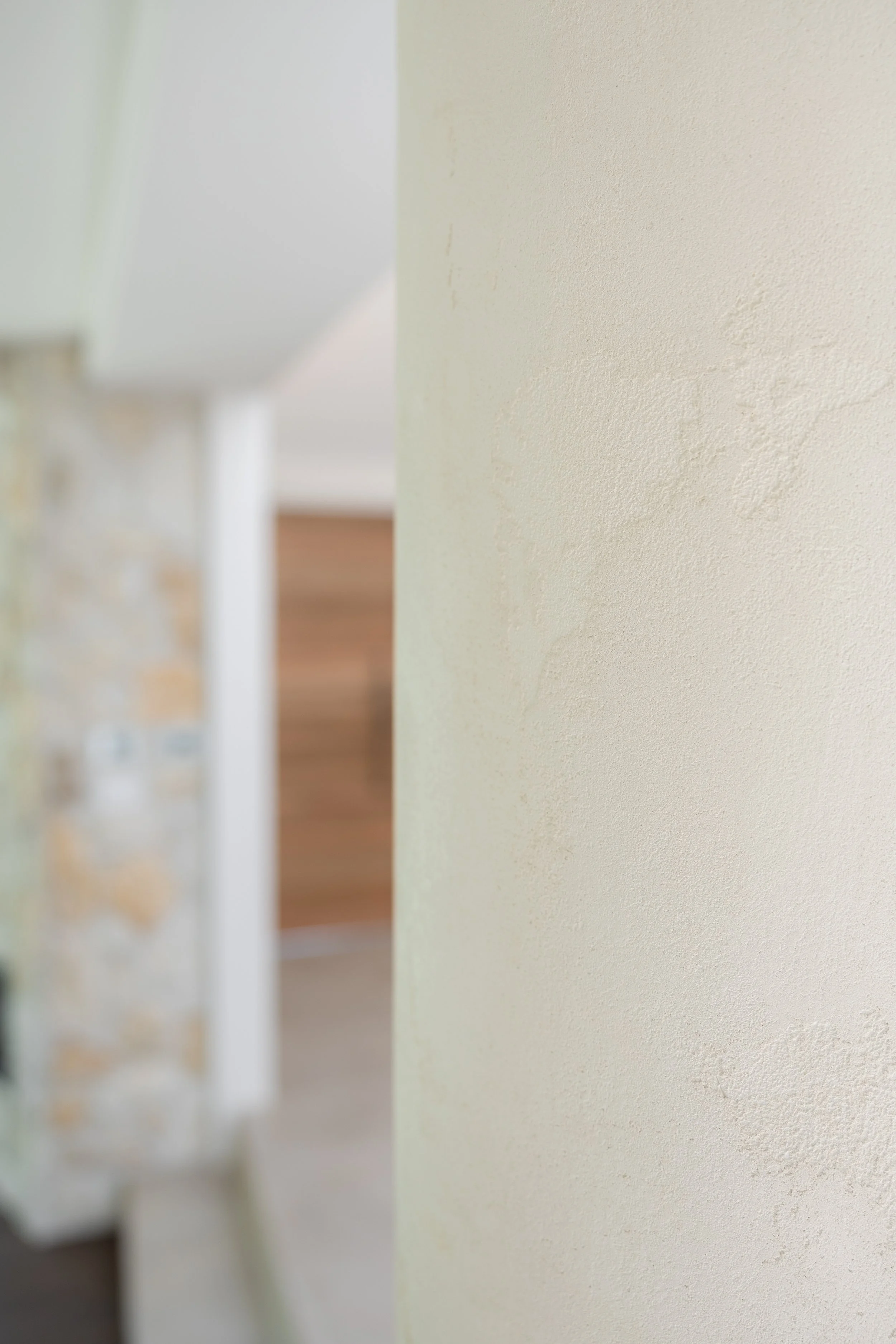 Close-up of a textured white wall with a partial view of a blurred fireplace in the background.