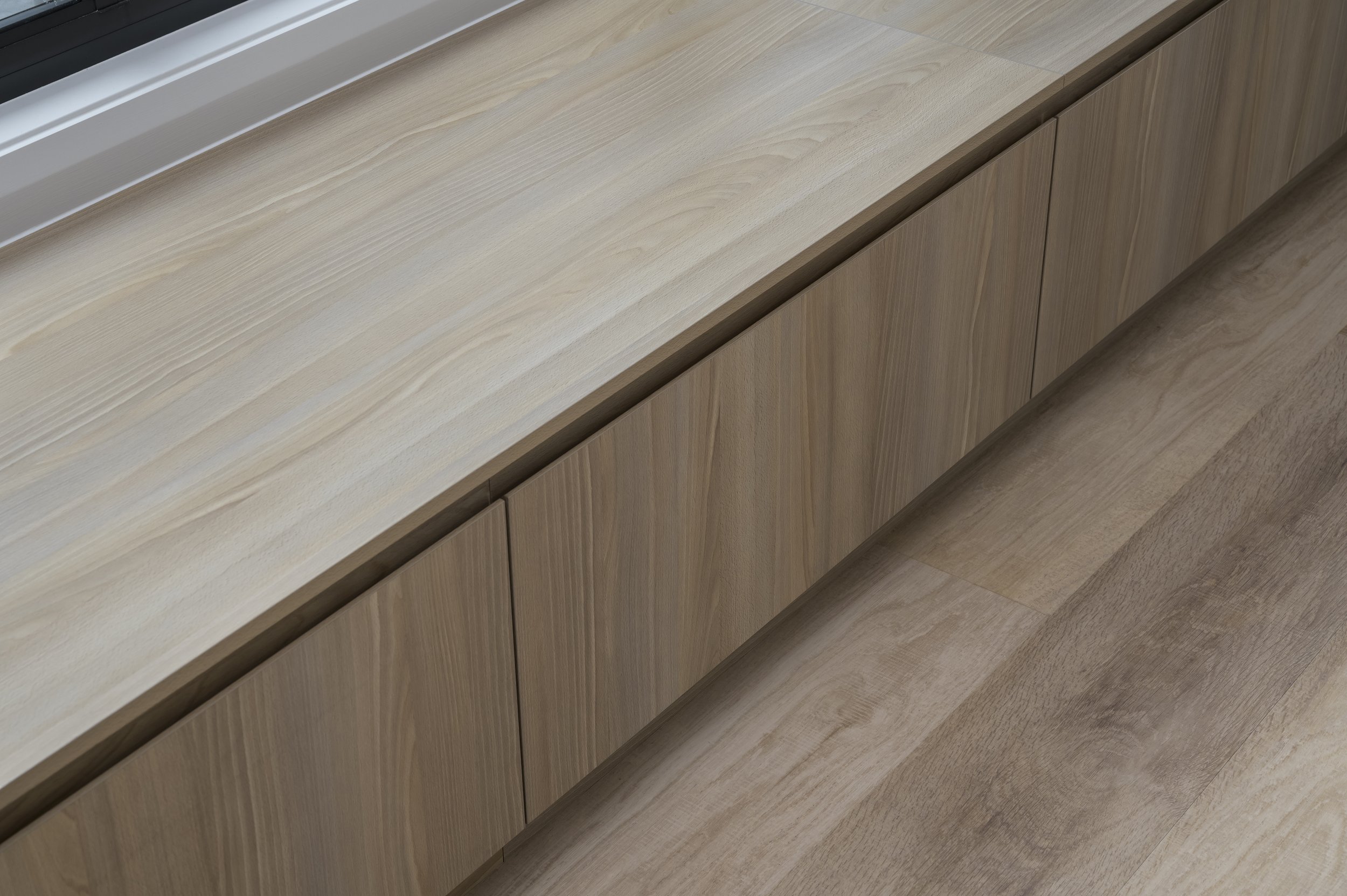 Wooden cabinet with three doors, below a window, with a light wood floor.